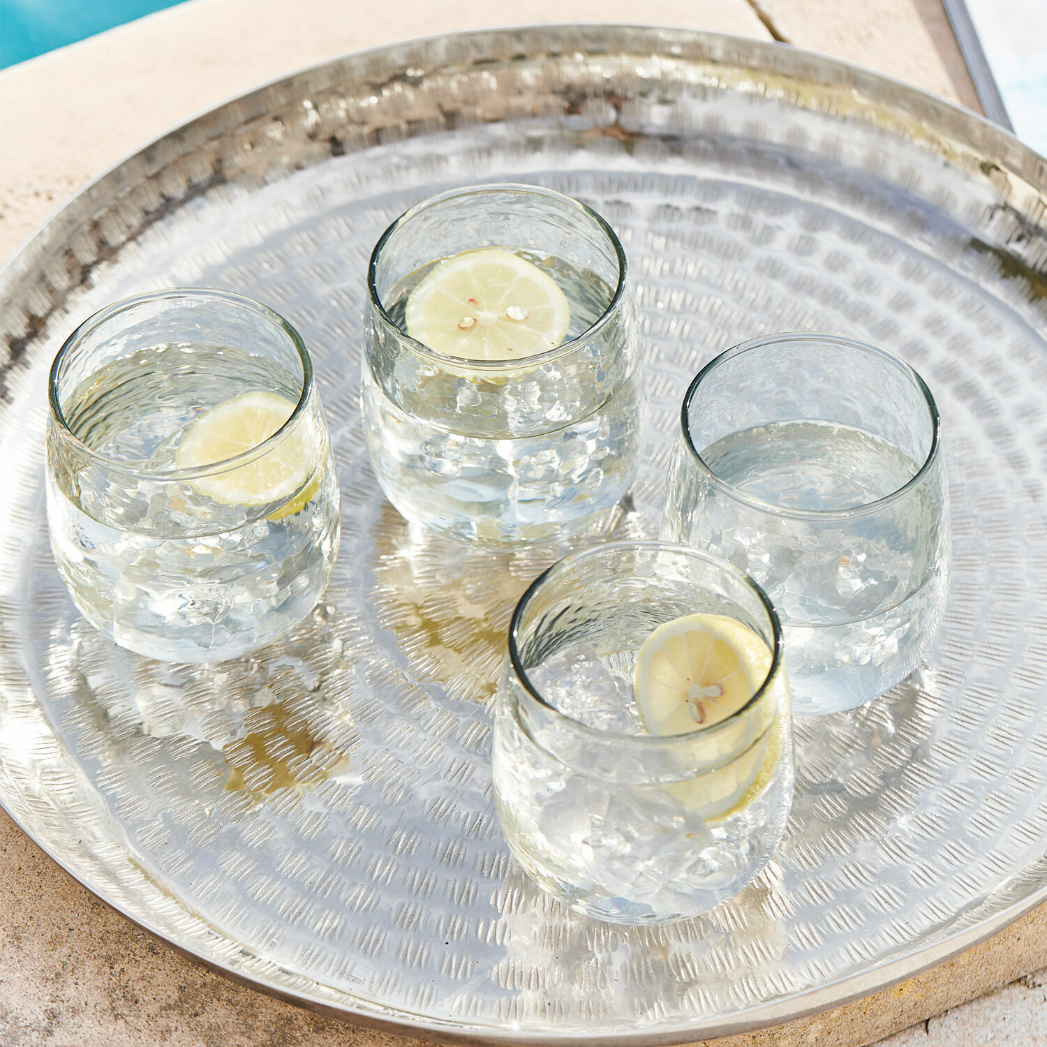 Bandeja metálica con cuatro vasos de agua y rodajas de limón junto a la piscina