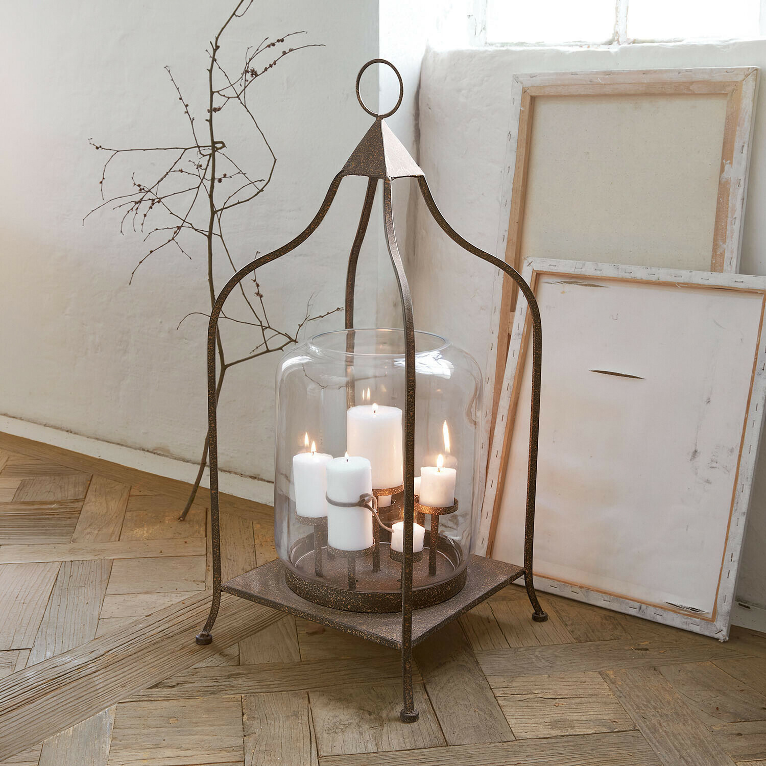 Farol Ilana Linterna de metal con pantalla de vidrio transparente y velas blancas sobre suelo de madera