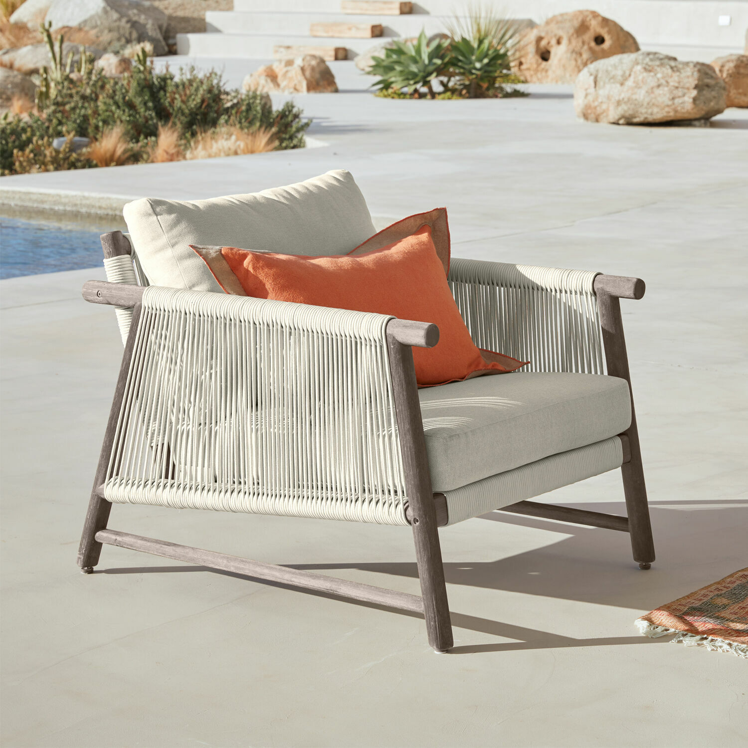 Sillón de exterior de madera y cuerda beige con cojín naranja, mueble para terraza