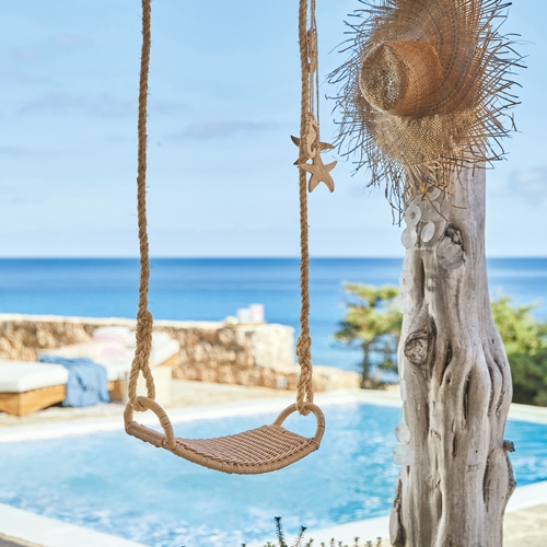 Columpio de cuerda trenzada frente a piscina con vista al mar, decoración veraniega
