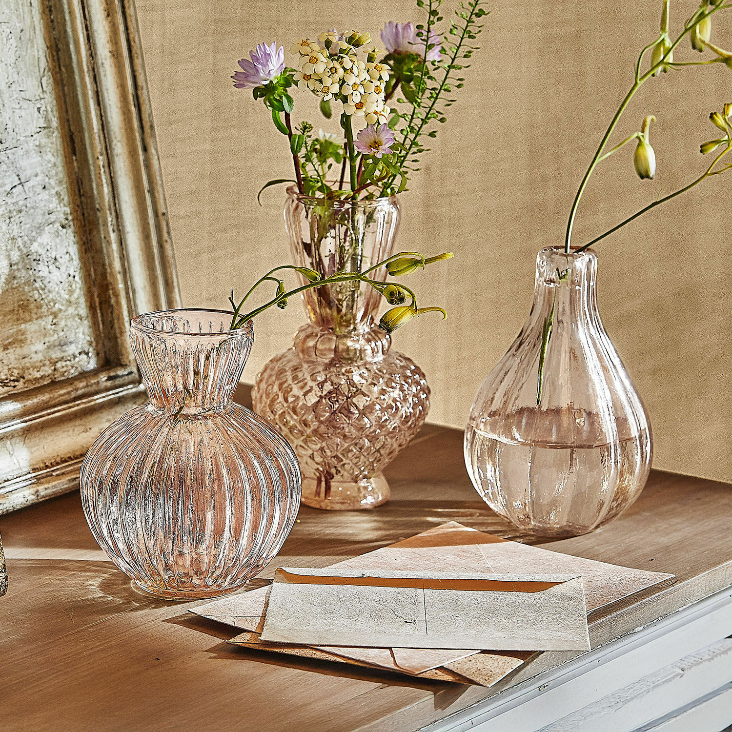 Set de 3 jarrones Faunelle Tres jarrones de vidrio transparente con flores sobre una mesa de madera en estilo vintage