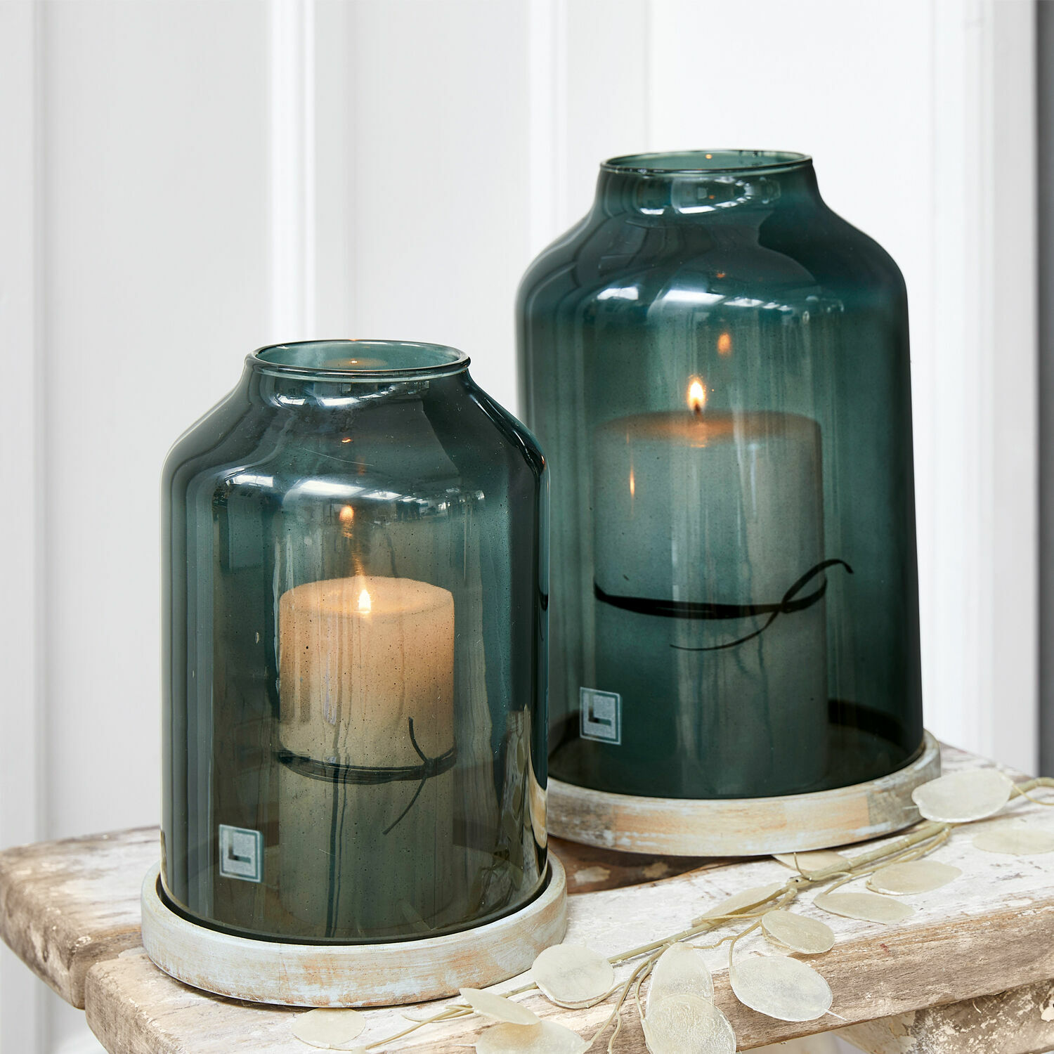 Set de 2 linternas Heavenly Dos faroles de vidrio verde con velas blancas sobre mesa de madera, decoración para interiores