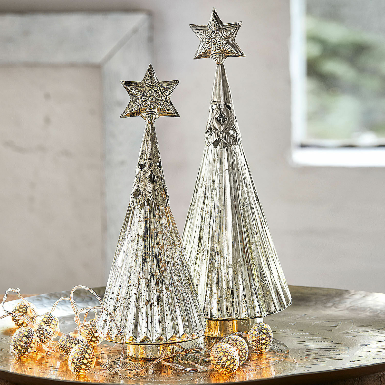 Set de 2 árboles de Navidad decorativos Lillemor Dos árboles navideños decorativos de metal plateado con estrellas en la cima sobre mesa festiva con luces LED