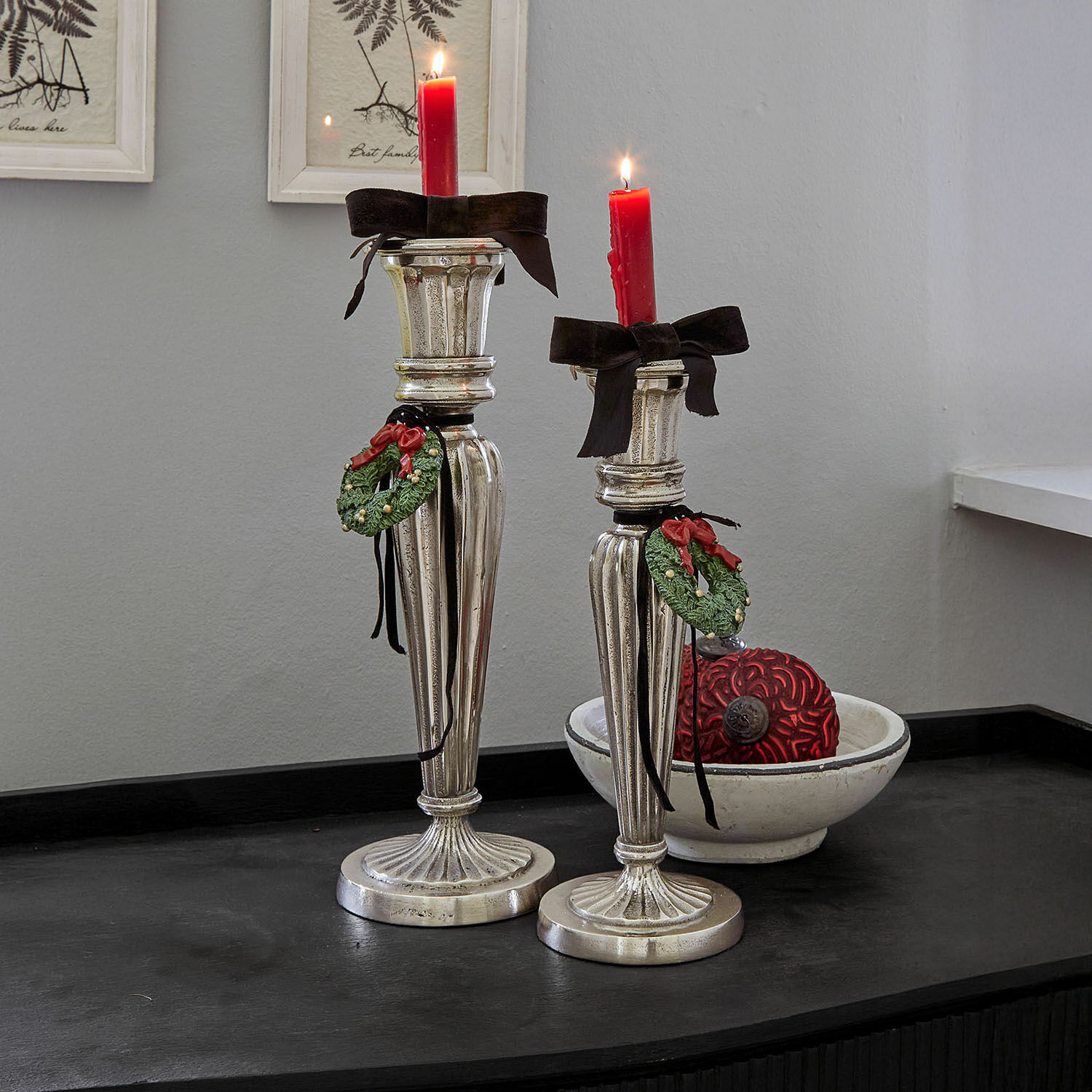 Set de 2 candeleros Zahfira Dos candelabros plateados con velas rojas y decoraciones de corona verde sobre superficie negra