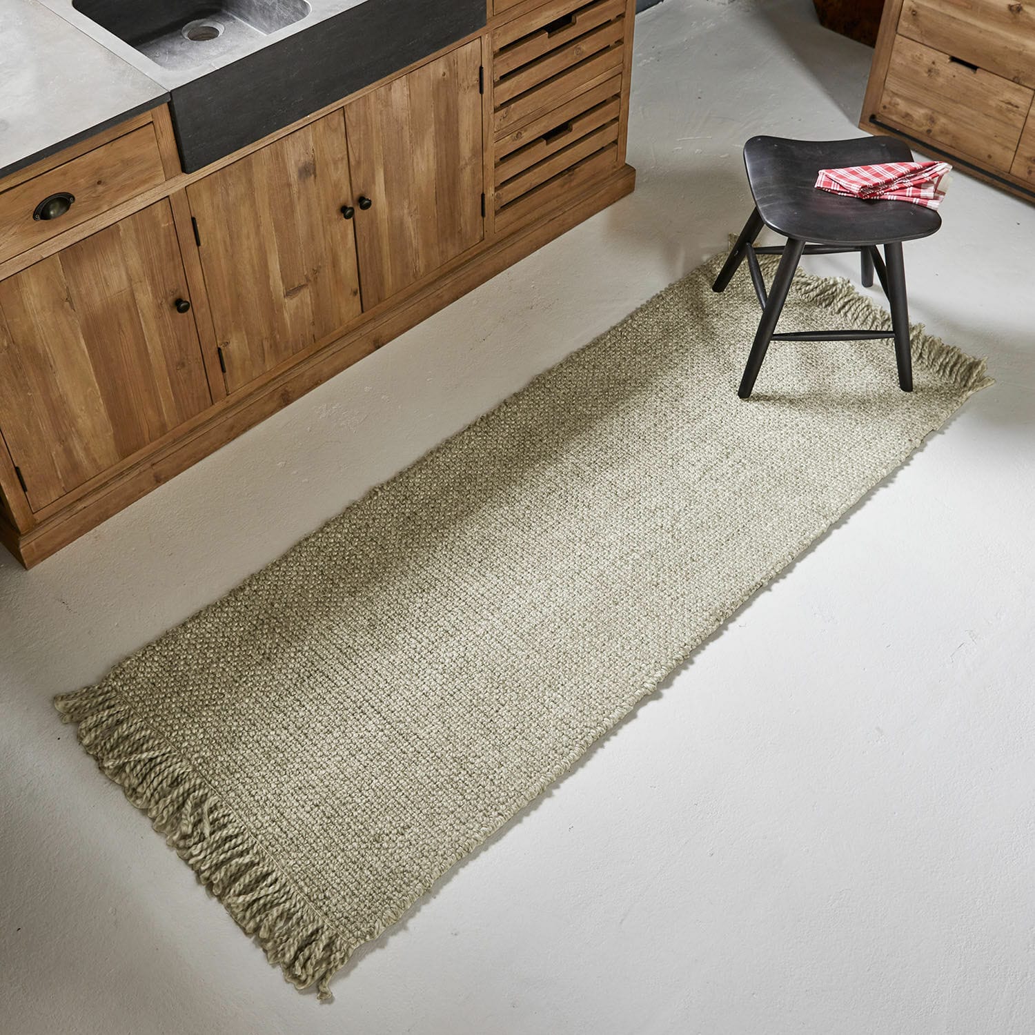 Alfombra Maravéa Alfombra beige con flecos de material natural en suelo de cocina con muebles de madera