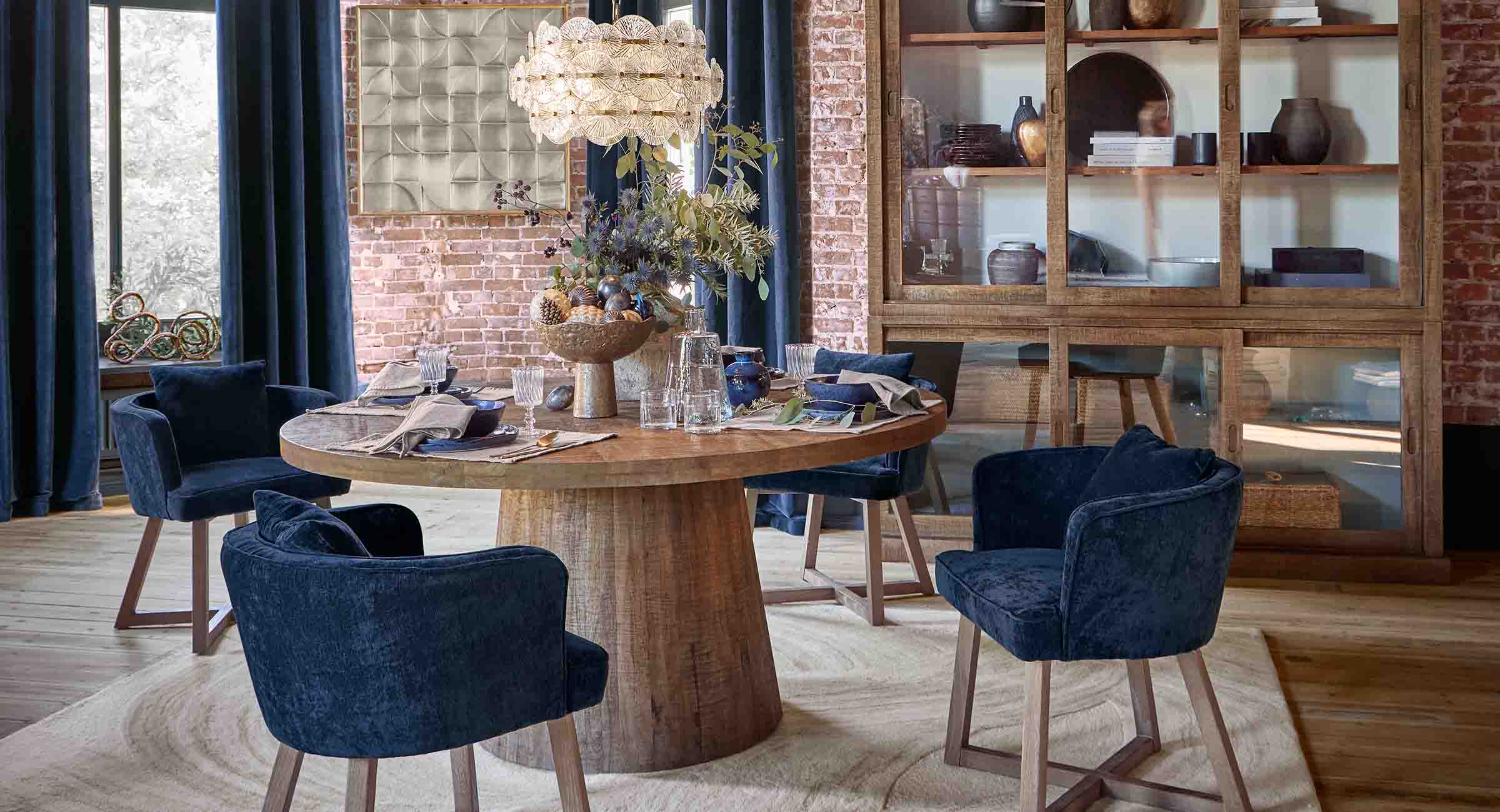 Comedor con mesa redonda de madera y sillas de terciopelo azul marino en estilo loft