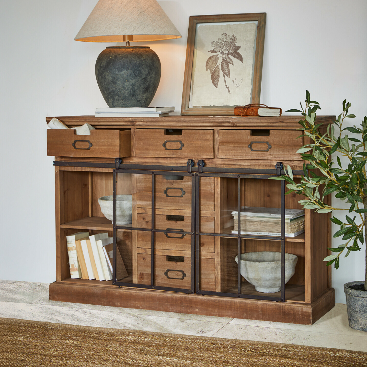 Aparador Finegand Aparador de madera con cajones y puertas de cristal, decorado con lámpara y planta, estilo rústico