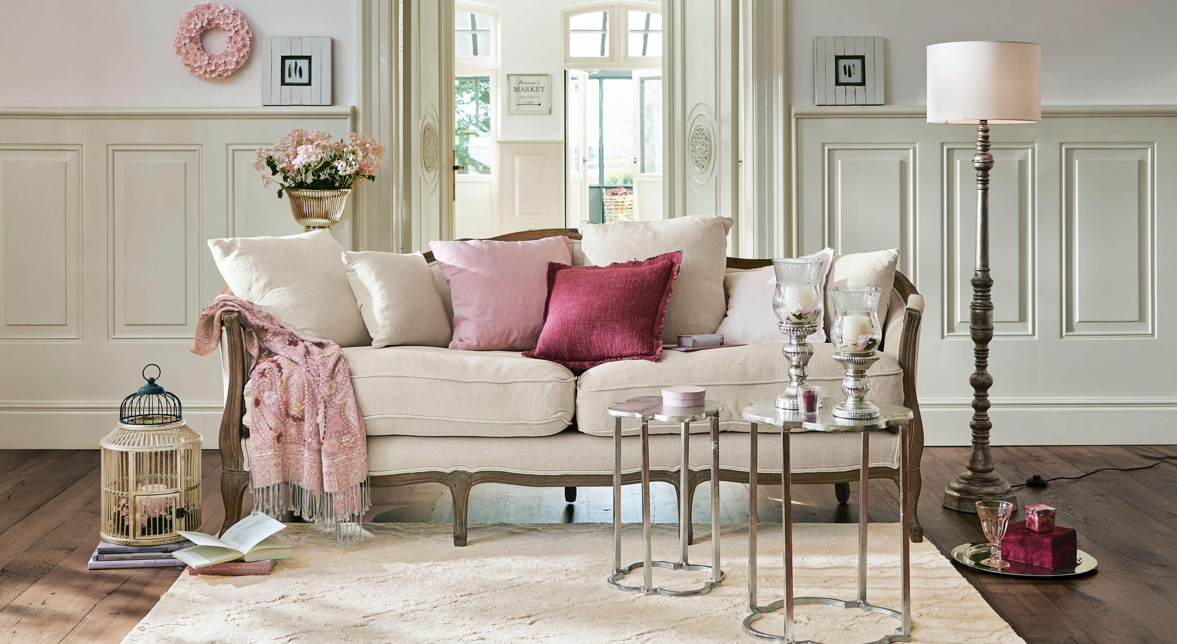 Sofá beige con marco de madera y cojines rosas en salón elegante con decoraciones