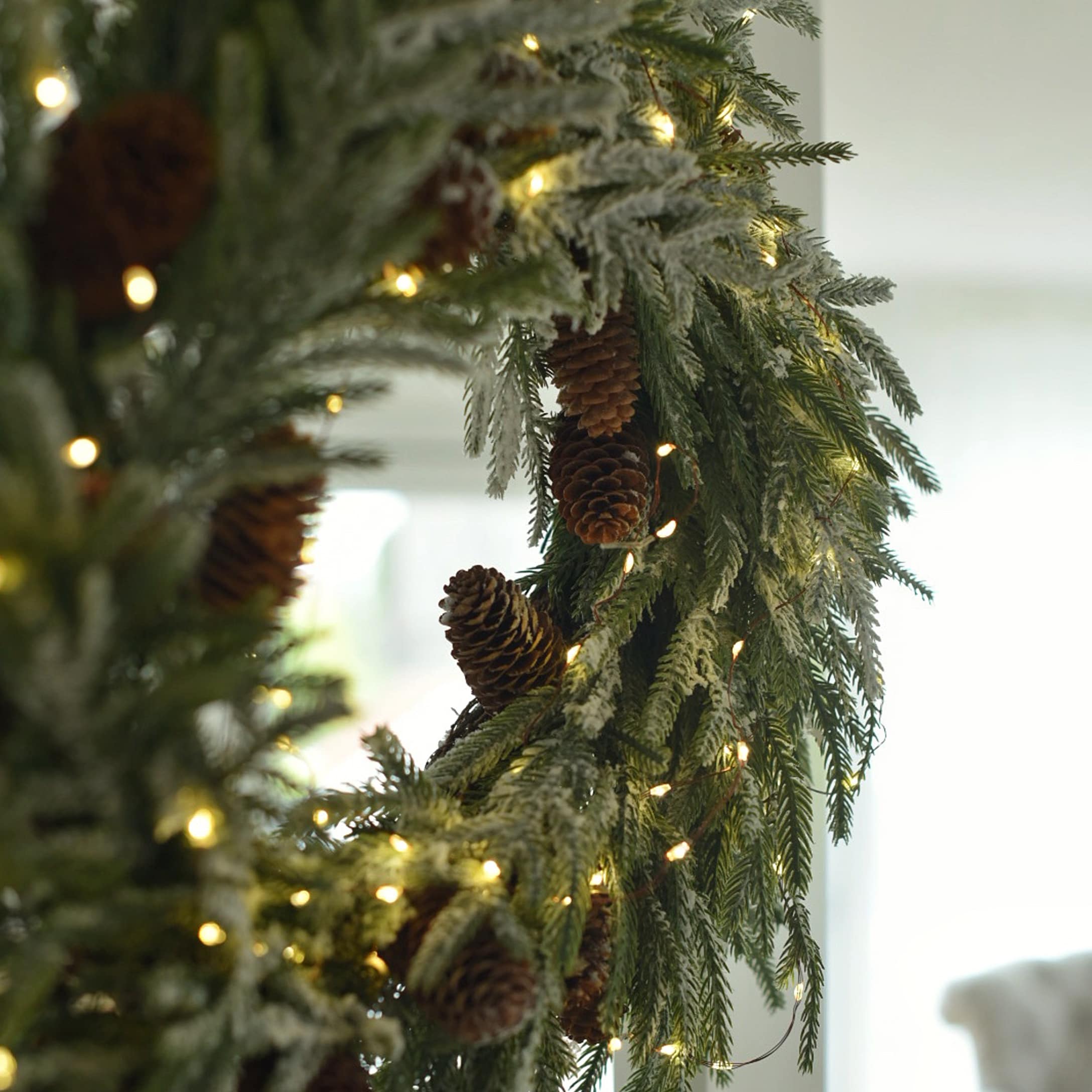 Corona navideña de ramas verdes con piñas y luces LED cálidas para decoración invernal