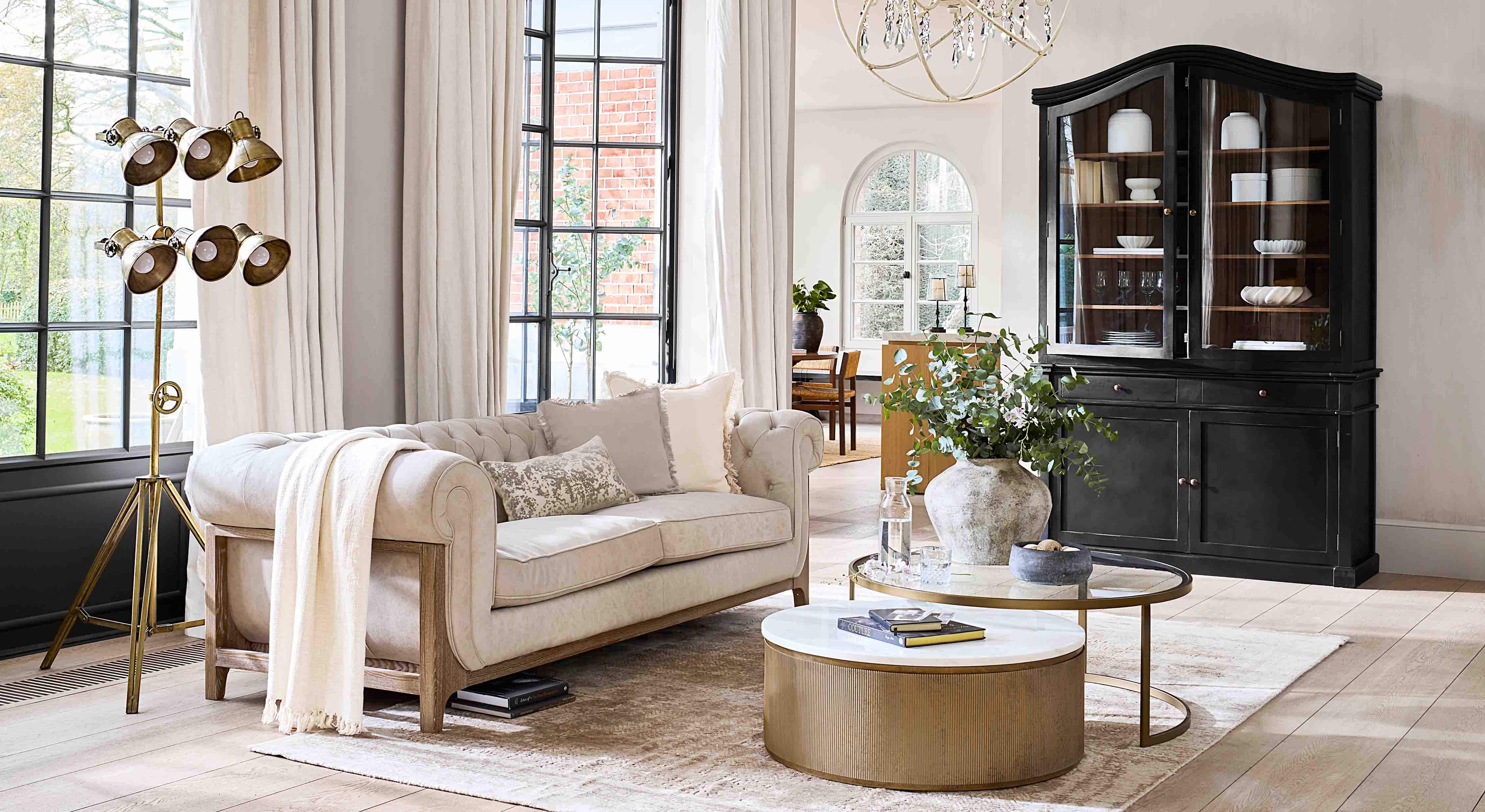 Sofá beige con marco de madera en salón luminoso con vitrina negra y lámpara dorada de pie