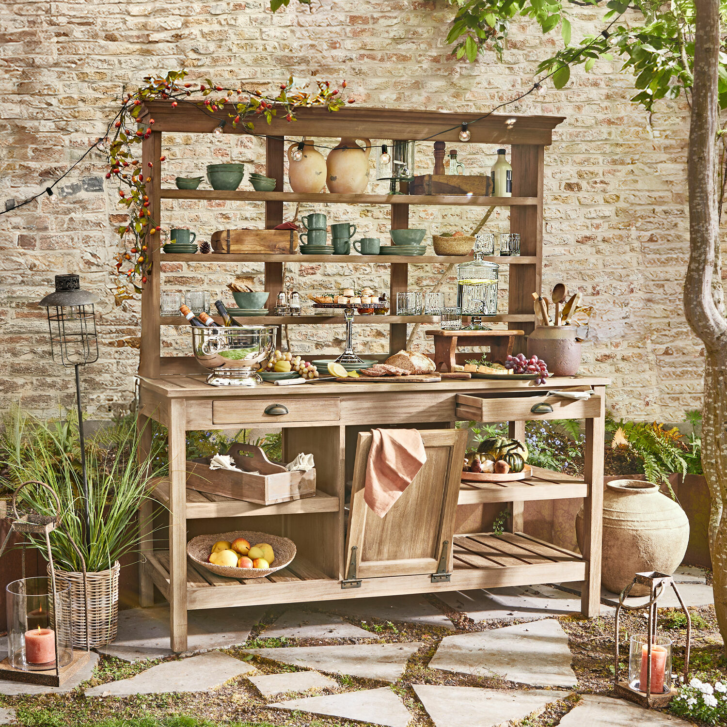 Armario de jardín Fallon Mueble de jardín de madera con estantes y cajones, decorado con vajilla y comida en patio
