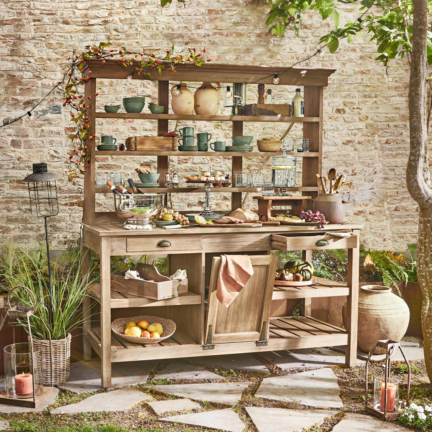 Armario de jardín Fallon Mueble de jardín de madera con estantes y cajones, decorado con vajilla y comida en patio