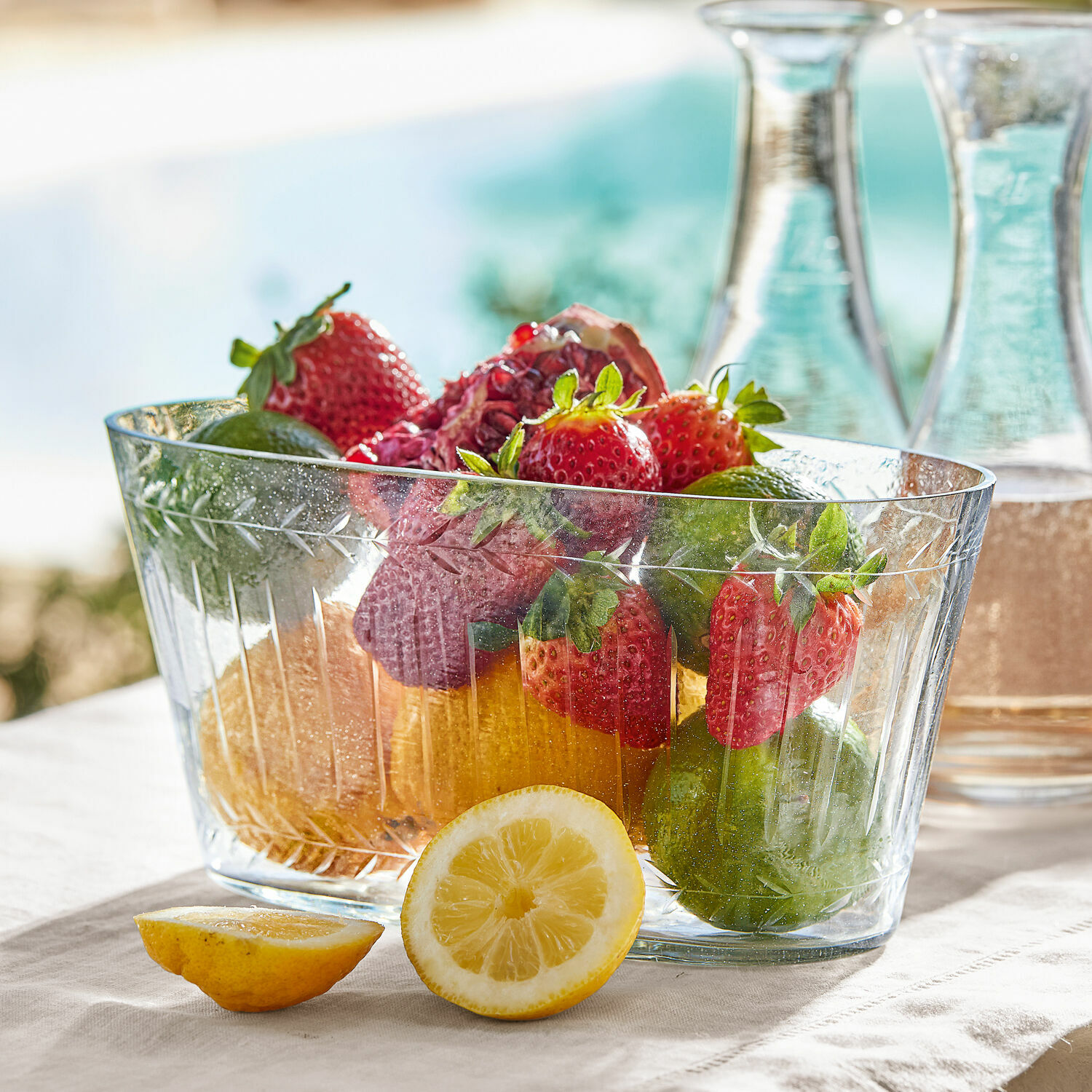 Cuenco Malinda Cuenco de cristal transparente con fresas, limas y limón sobre mantel claro, decoración de mesa