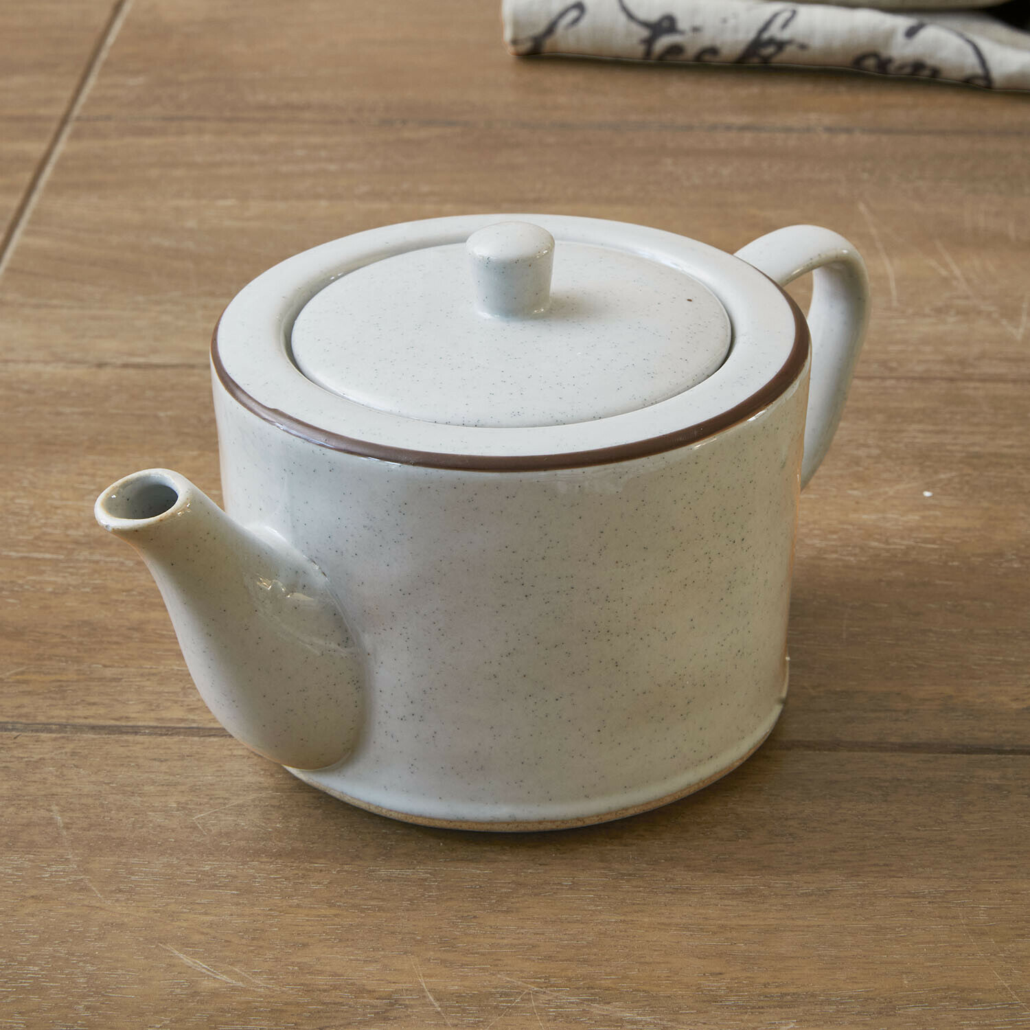 Tetera Biarré Tetera de cerámica blanca con borde marrón sobre mesa de madera para preparar té