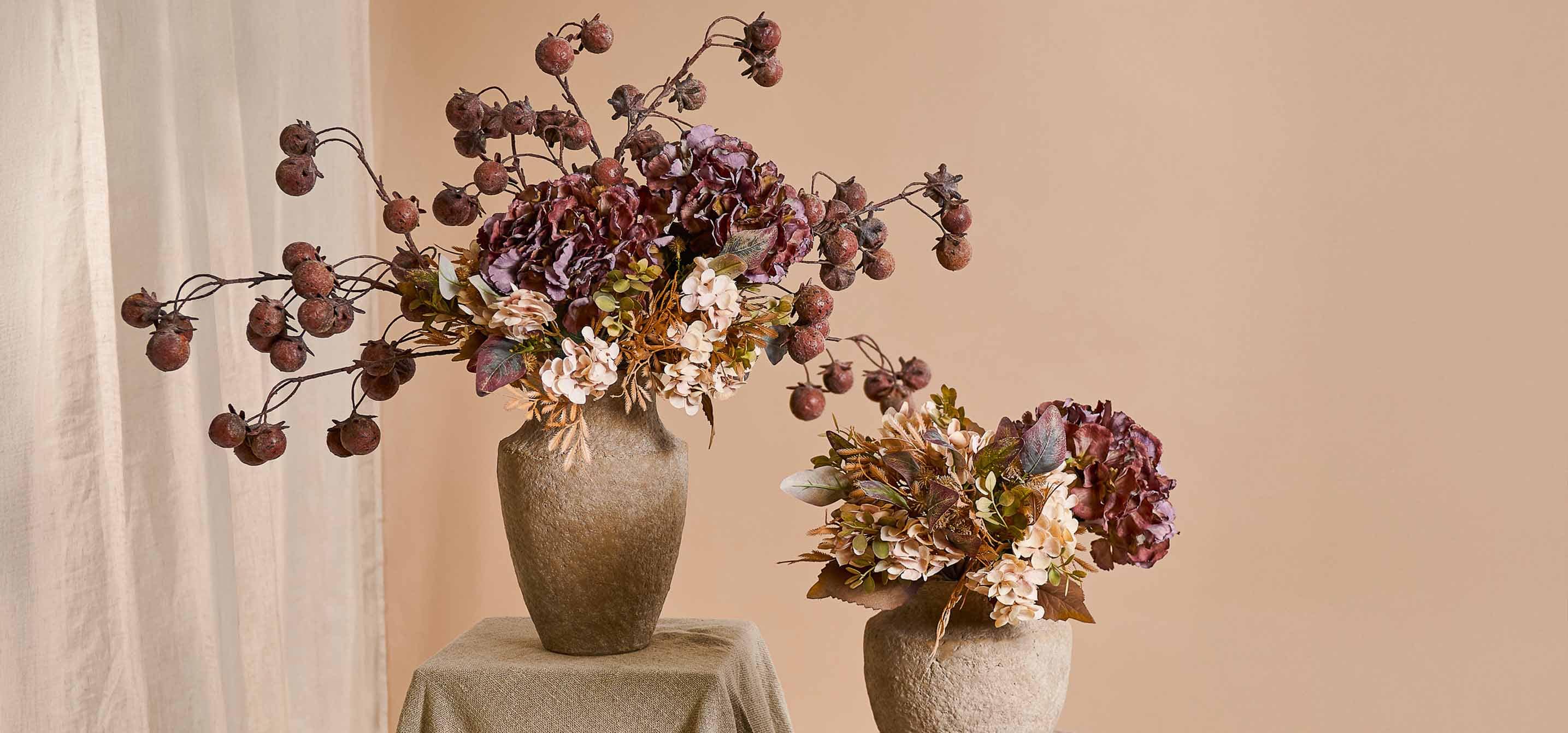 Dos jarrones decorativos de piedra beige con flores otoñales y frutos secos en tonos cálidos para decoración