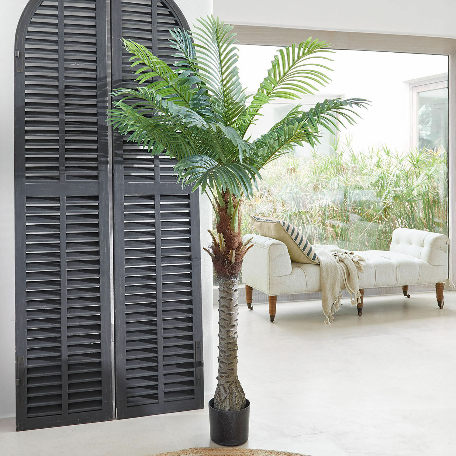 Planta decorativa en maceta Zephyriel Palma artificial en maceta negra en sala luminosa con sofá beige y ventana grande