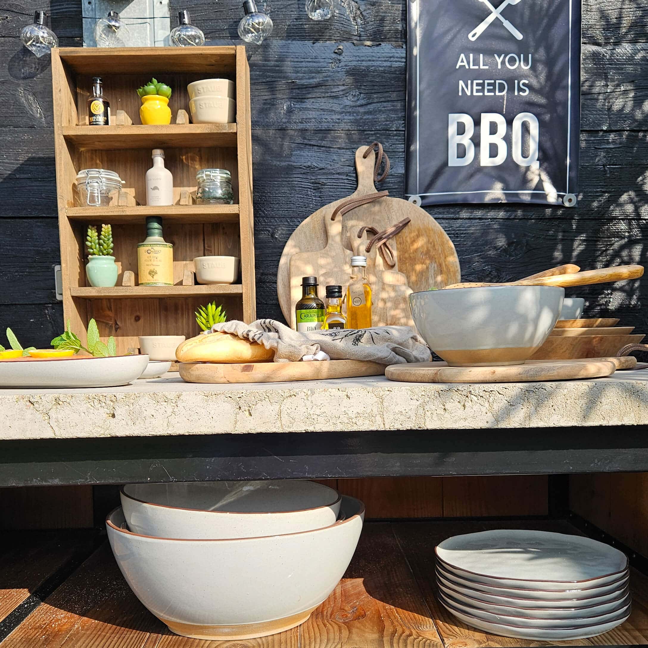 Conjunto de cuencos y platos de cerámica beige con tablas de cortar de madera y botellas de aceite en mesa de barbacoa