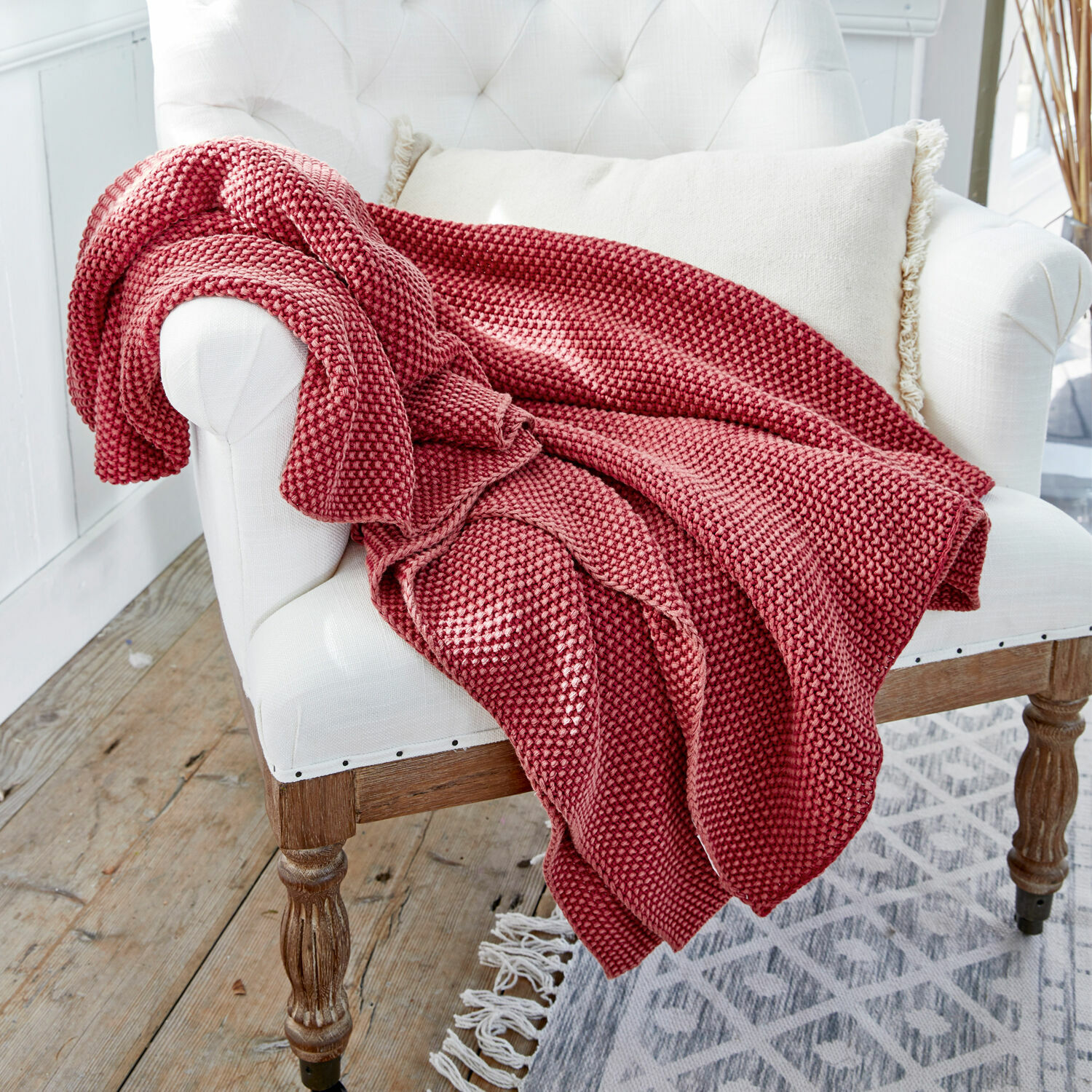 Plaid Amberley Manta roja tejida de material suave sobre sillón blanco en interior luminoso