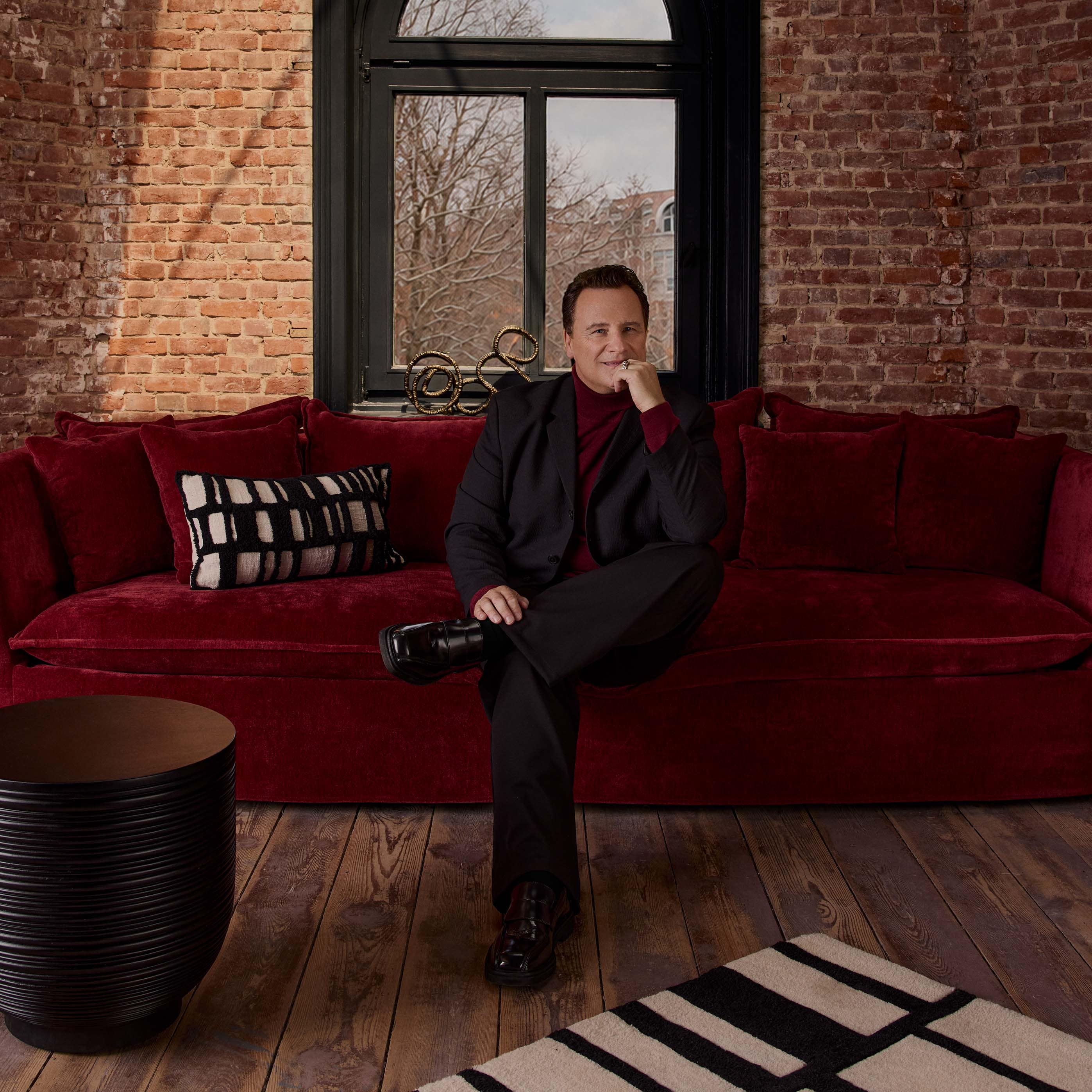 Sofá esquinero rojo de terciopelo con cojines y cojín decorativo blanco y negro en interior industrial