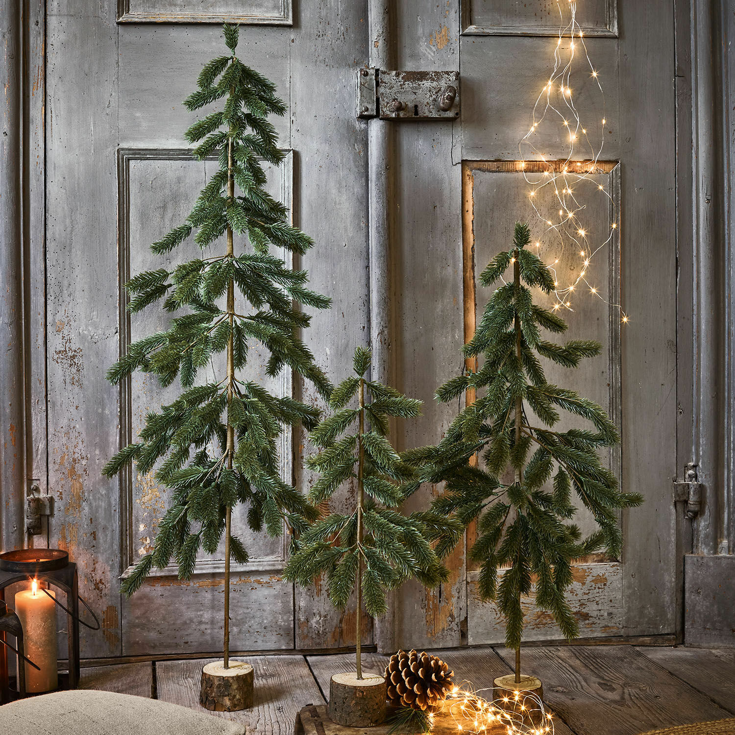 Set de 3 árboles de Navidad Lorin Tres árboles decorativos verdes con bases de madera, luces LED y piña decorativa en primer plano