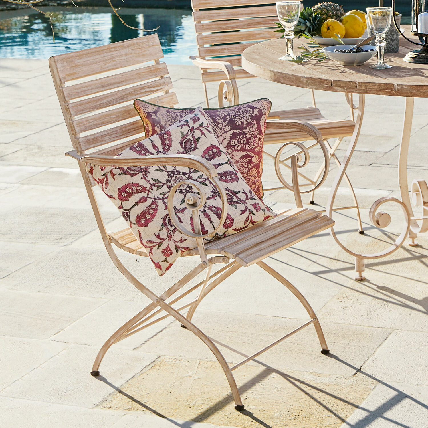 Silla de jardín de madera y metal claro con dos cojines decorativos con estampado floral rojo