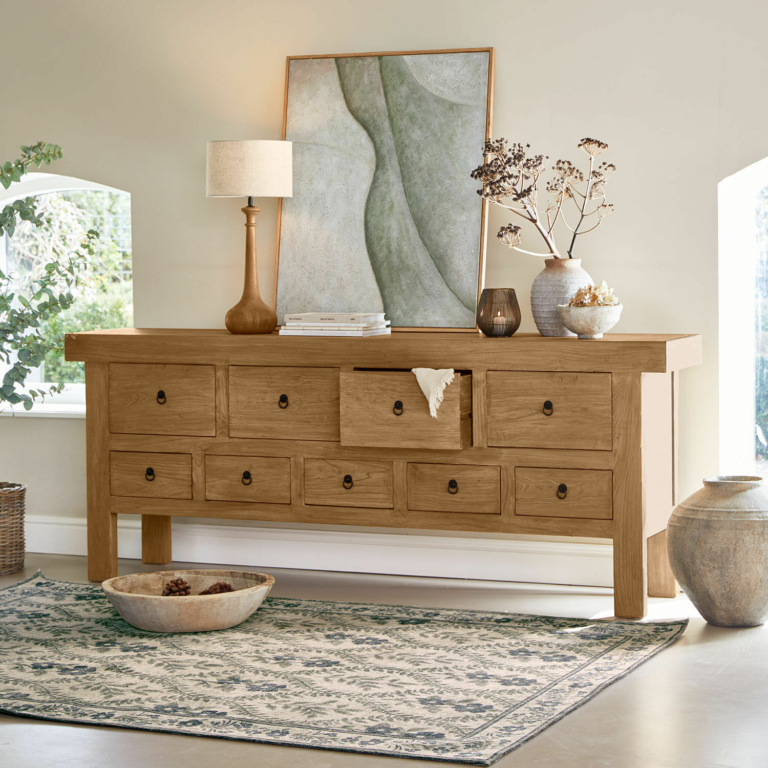 Aparador de madera natural con múltiples cajones, decorado con lámpara y jarrón en habitación luminosa