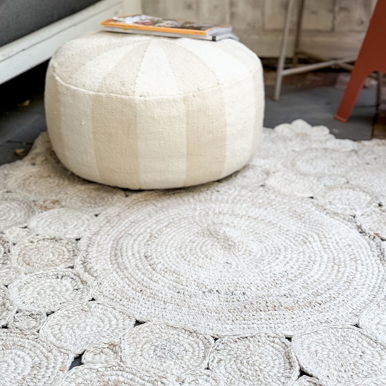 Puf redondo blanco de tela sobre alfombra tejida clara, decoración acogedora para salón
