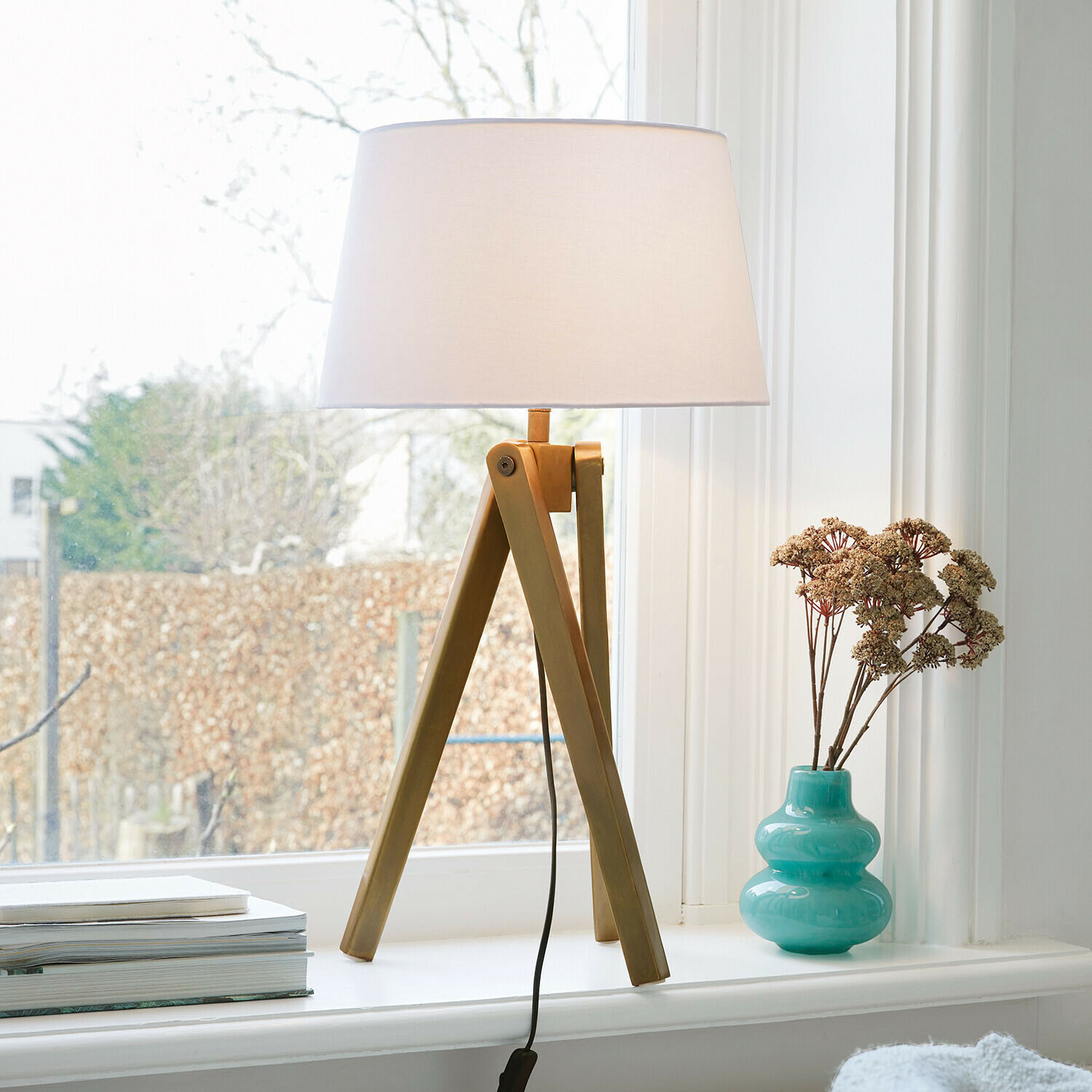 Lámpara de mesa Kelvio Lámpara de mesa con base de madera y pantalla blanca en el alféizar junto a un jarrón turquesa