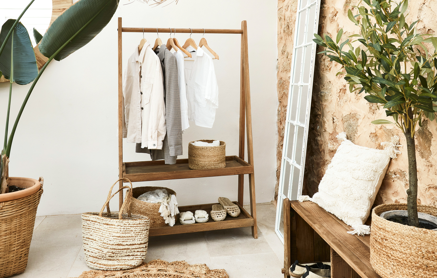 Perchero de madera con camisas claras y cestas de mimbre en interior estilo bohemio