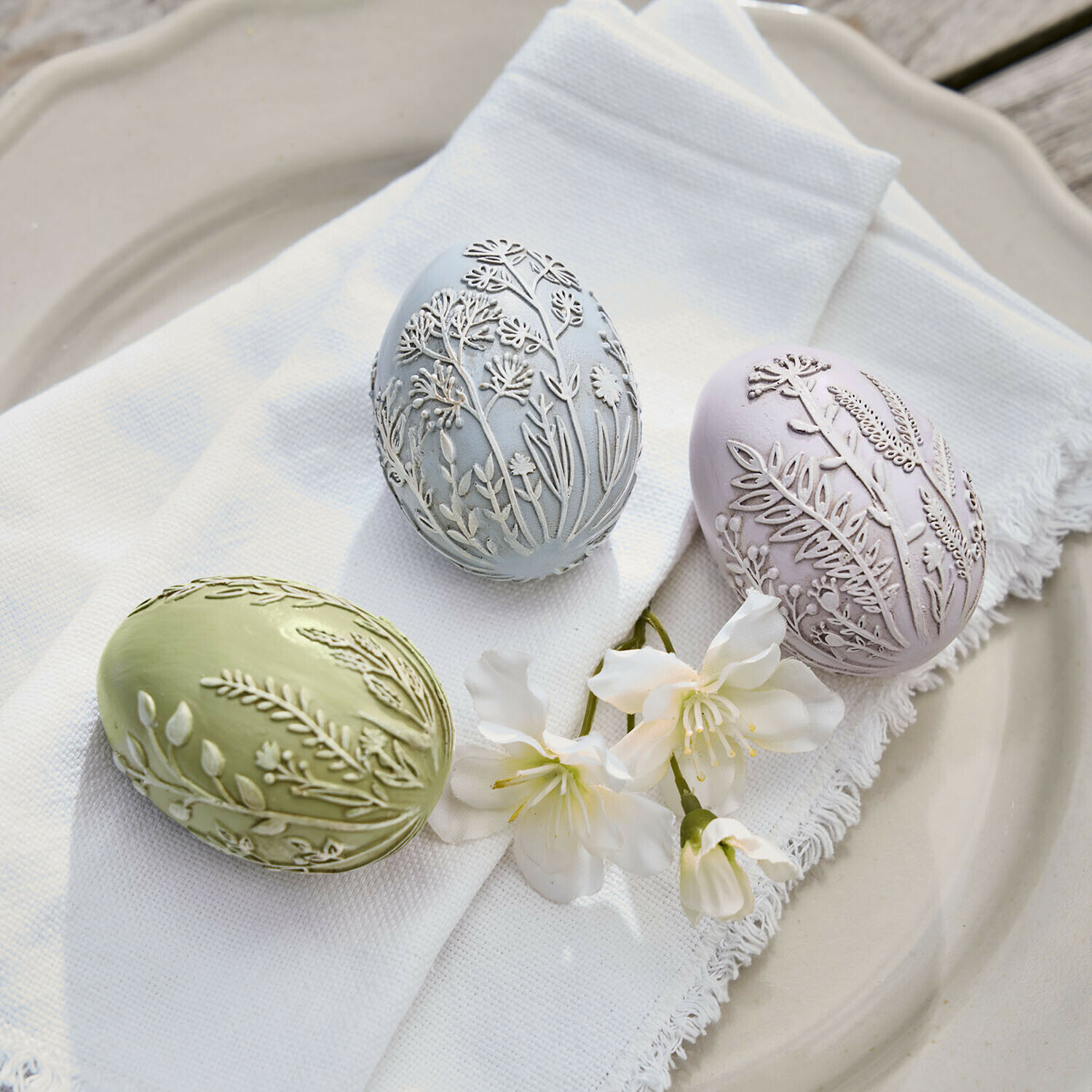 Set de 3 huevos de Pascua Fauverine Tres huevos decorativos en tonos pastel con relieve floral sobre tela blanca y flores en plato