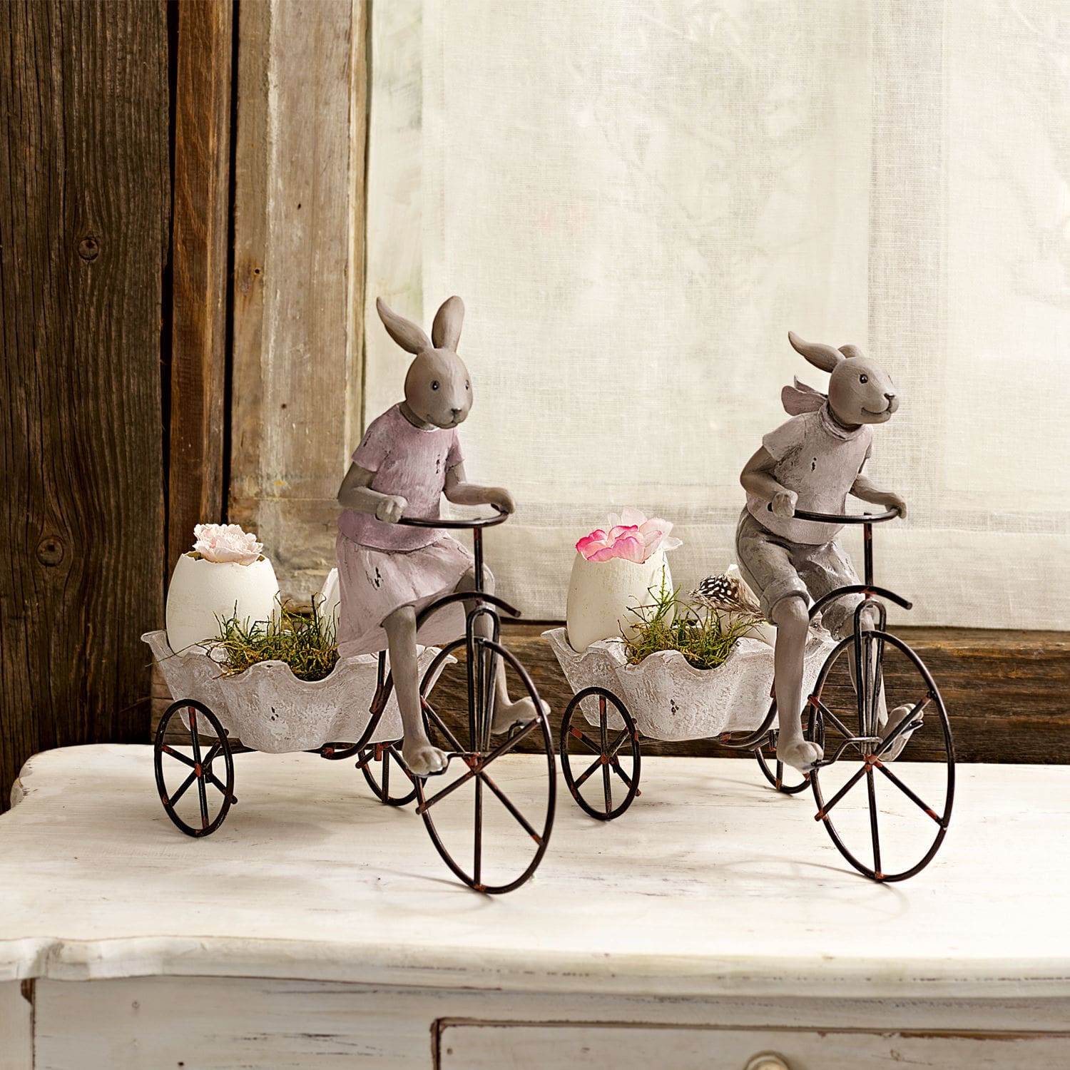 Figuras decorativas de conejos en bicicletas de metal con macetas blancas y flores sobre mesa