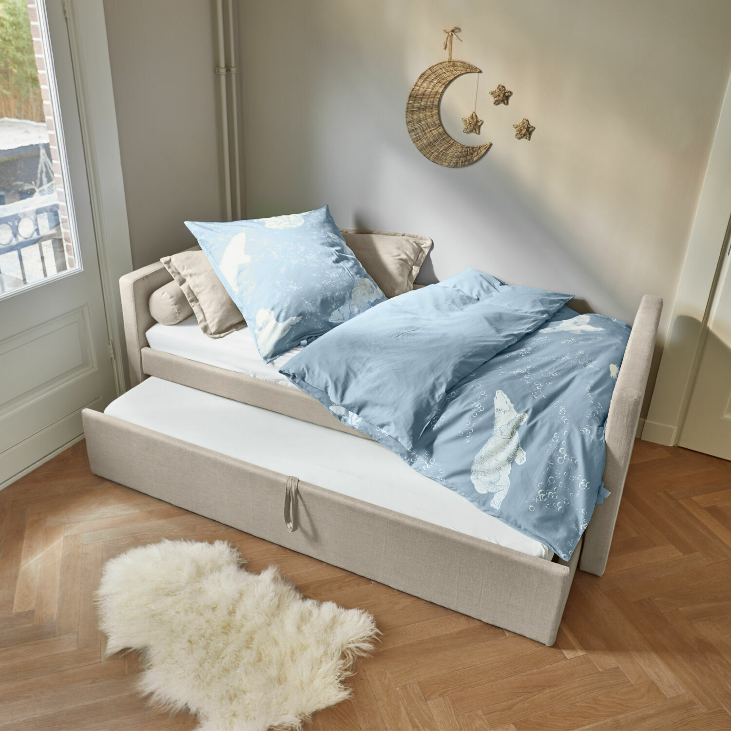 Cama Thistlewood Cama beige con colchón extraíble y ropa de cama azul con diseño de oso polar en habitación luminosa.