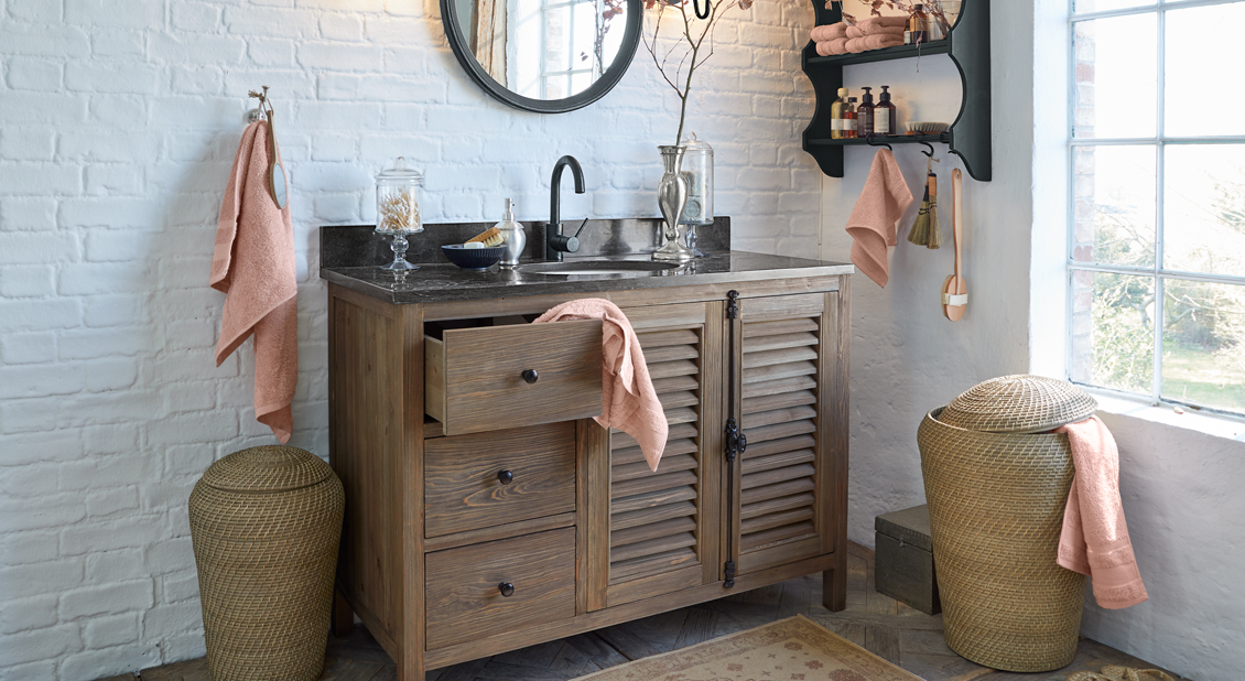 Baño con mueble de madera, encimera negra y toallas terracota, decoración natural