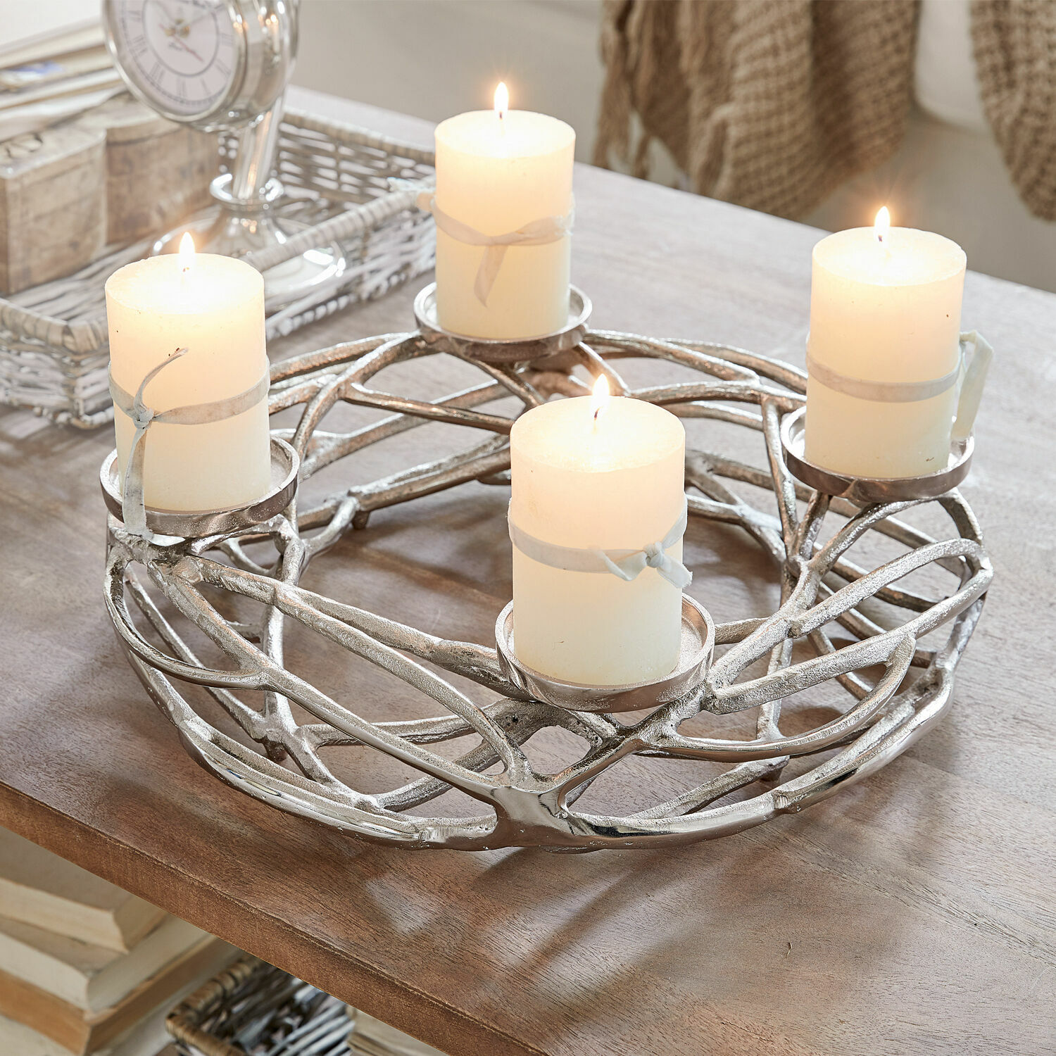 Corona de velas Coldfield Candelabro metálico plateado con cuatro velas blancas encendidas sobre mesa de madera, decoración interior