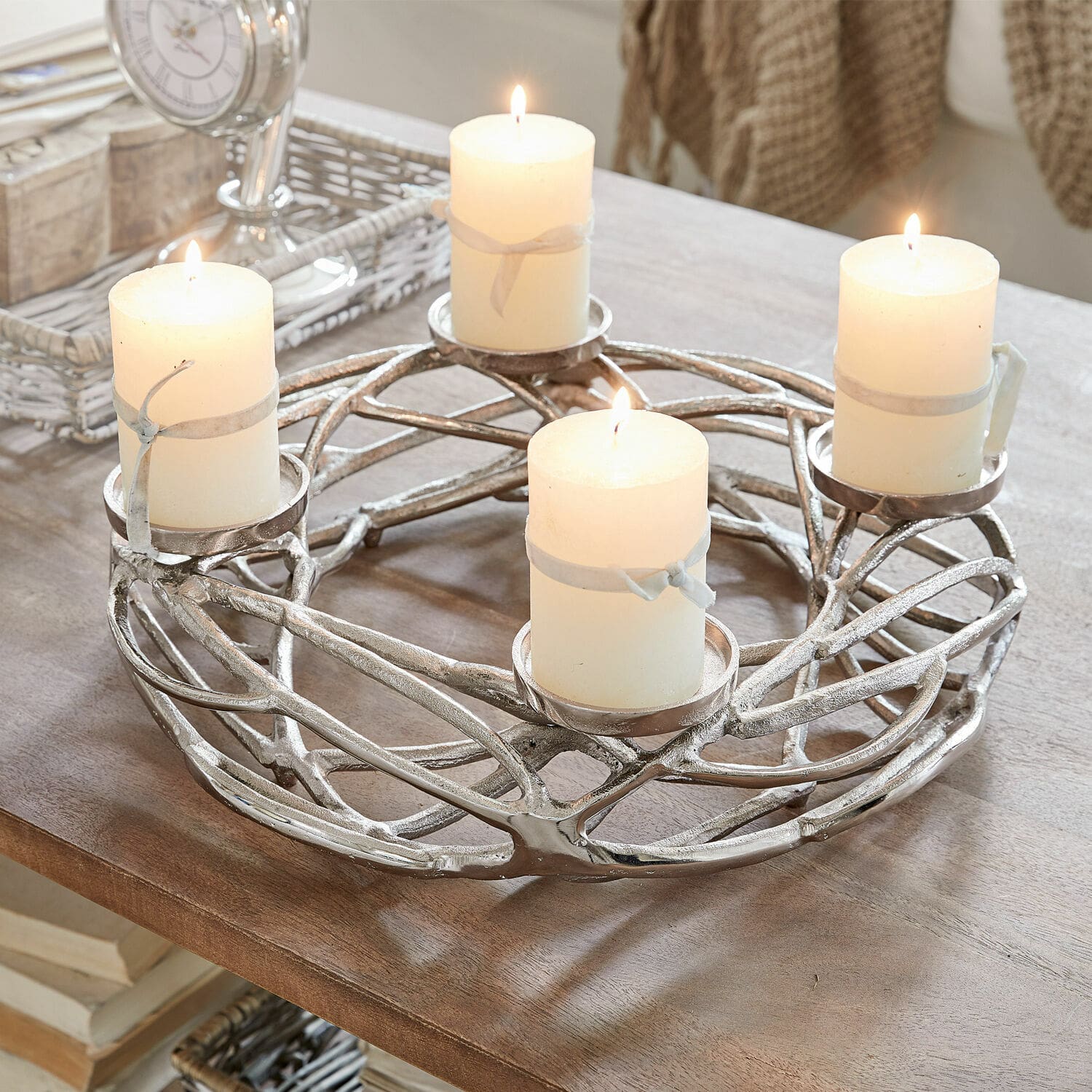 Corona de velas Coldfield Candelabro metálico plateado con cuatro velas blancas encendidas sobre mesa de madera, decoración interior