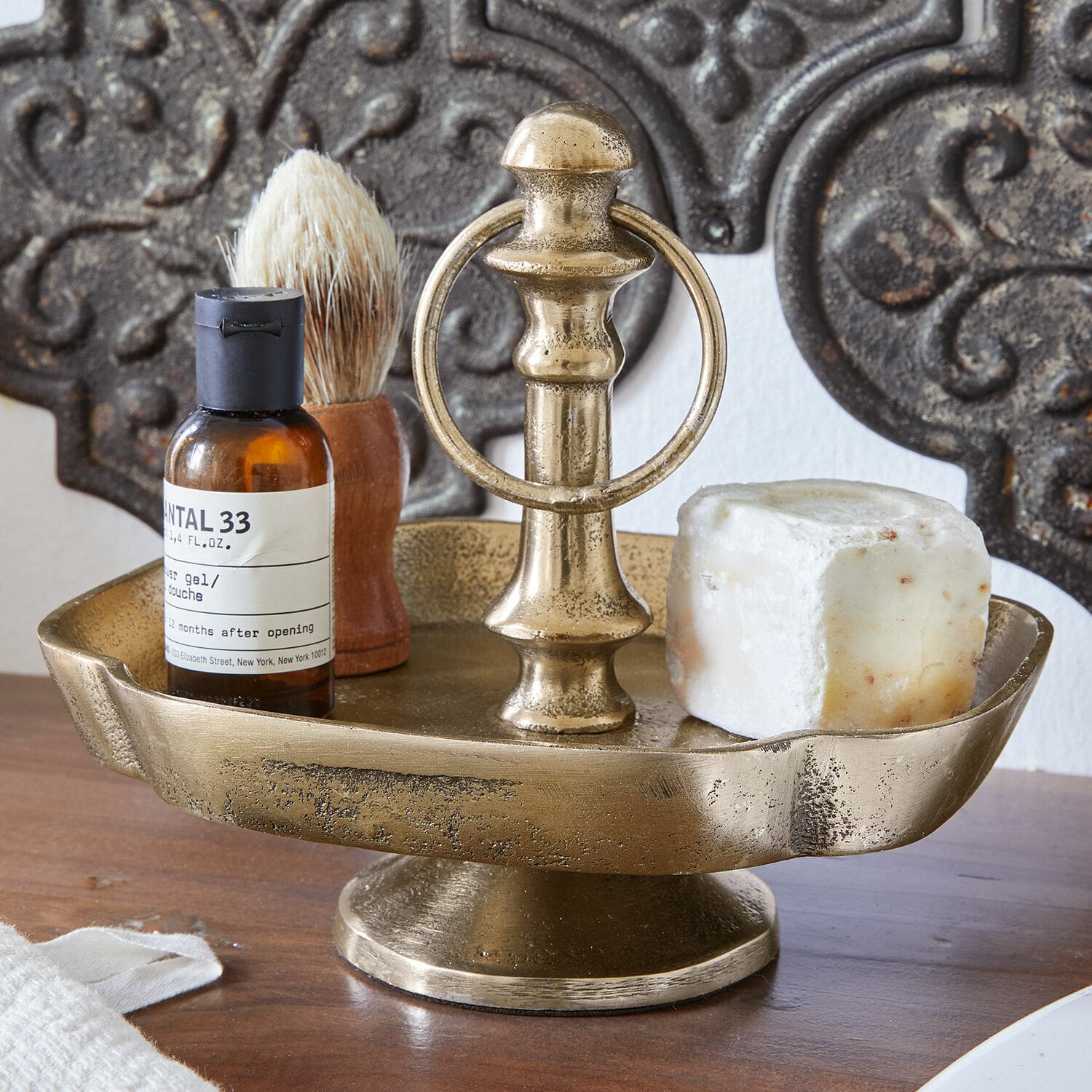 Bandeja con pie Frinesto Jabonera metálica dorada con asa, jabón y accesorios de afeitado sobre mesa de madera