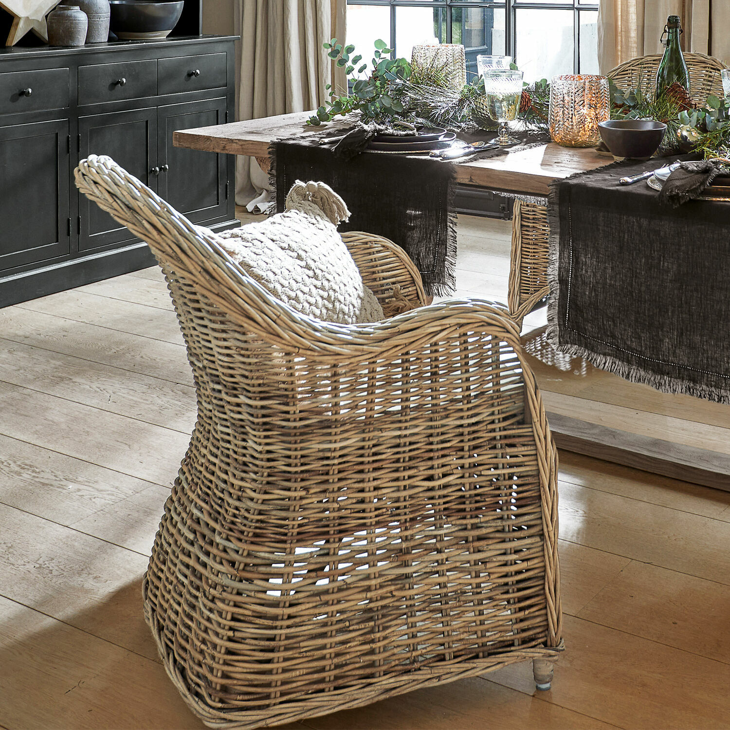 Silla de ratán natural con cojín junto a mesa de madera en comedor luminoso