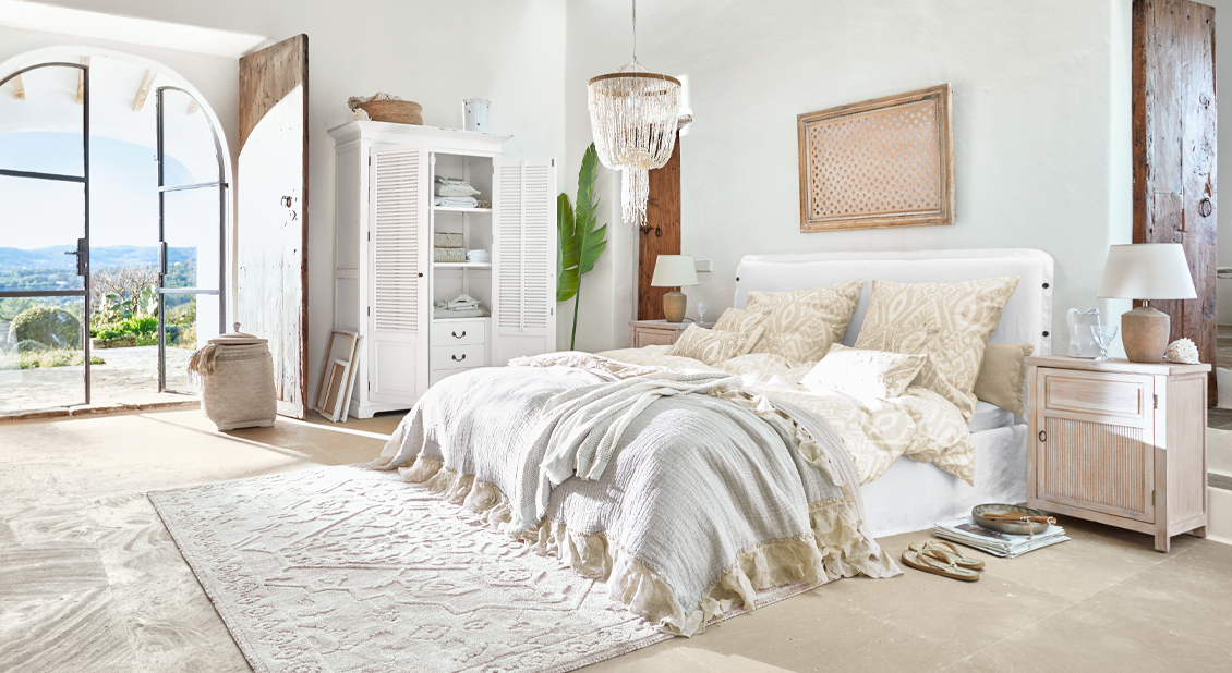 Dormitorio luminoso con cama blanca, ropa de cama beige y muebles de madera rústicos