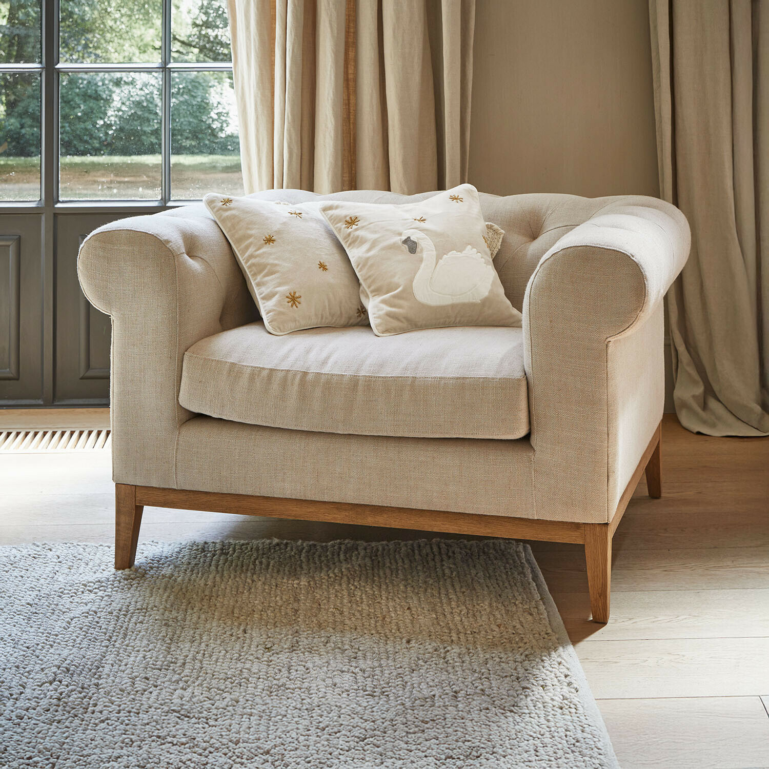 Sillón Fairbourne Sofá beige de tela con base de madera y dos cojines decorativos con bordado de cisne
