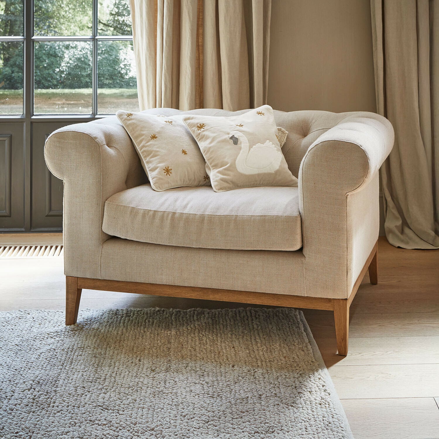 Sillón Fairbourne Sofá beige de tela con base de madera y dos cojines decorativos con bordado de cisne