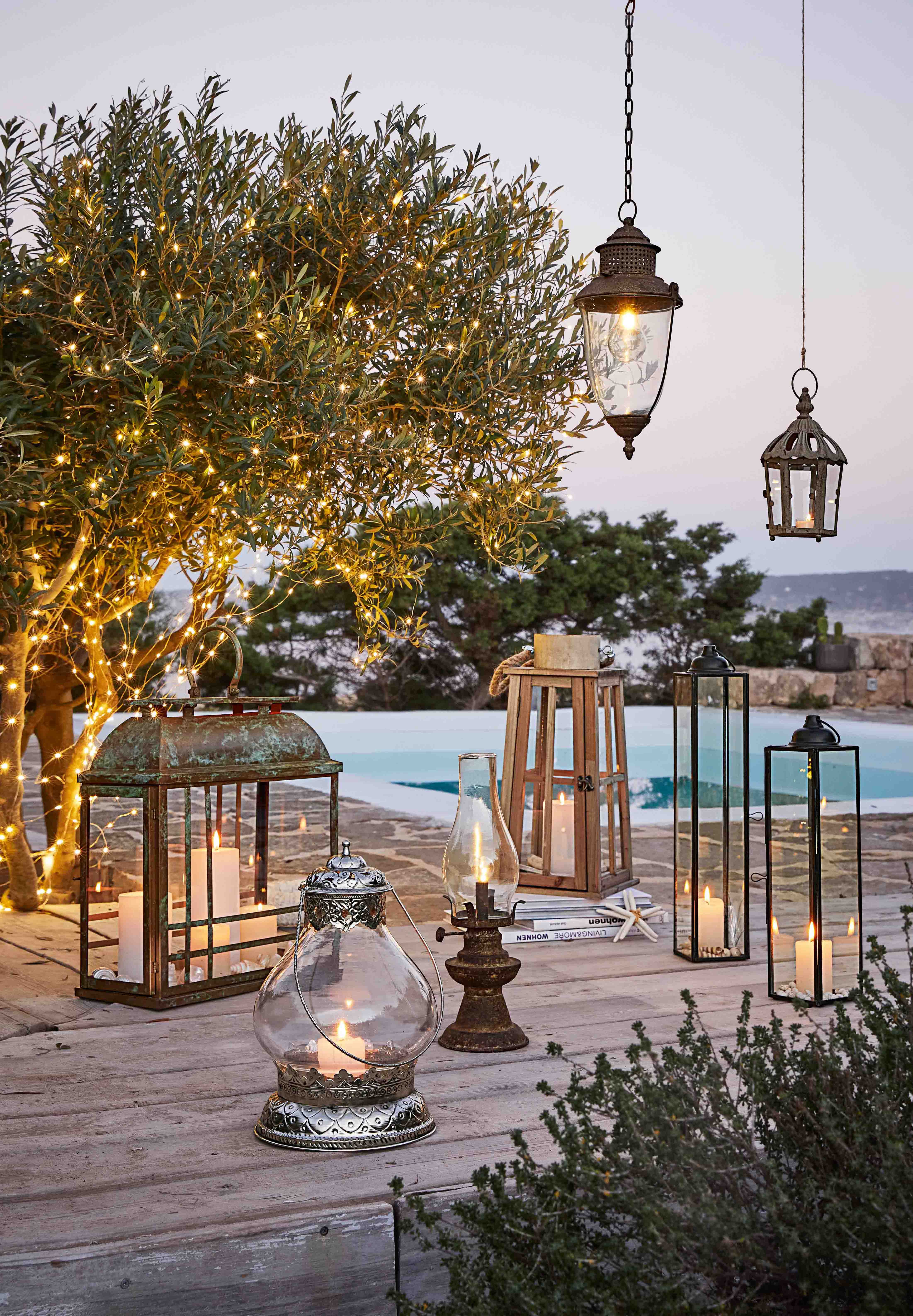 Conjunto de faroles y velas en terraza de madera con árbol decorado con luces LED