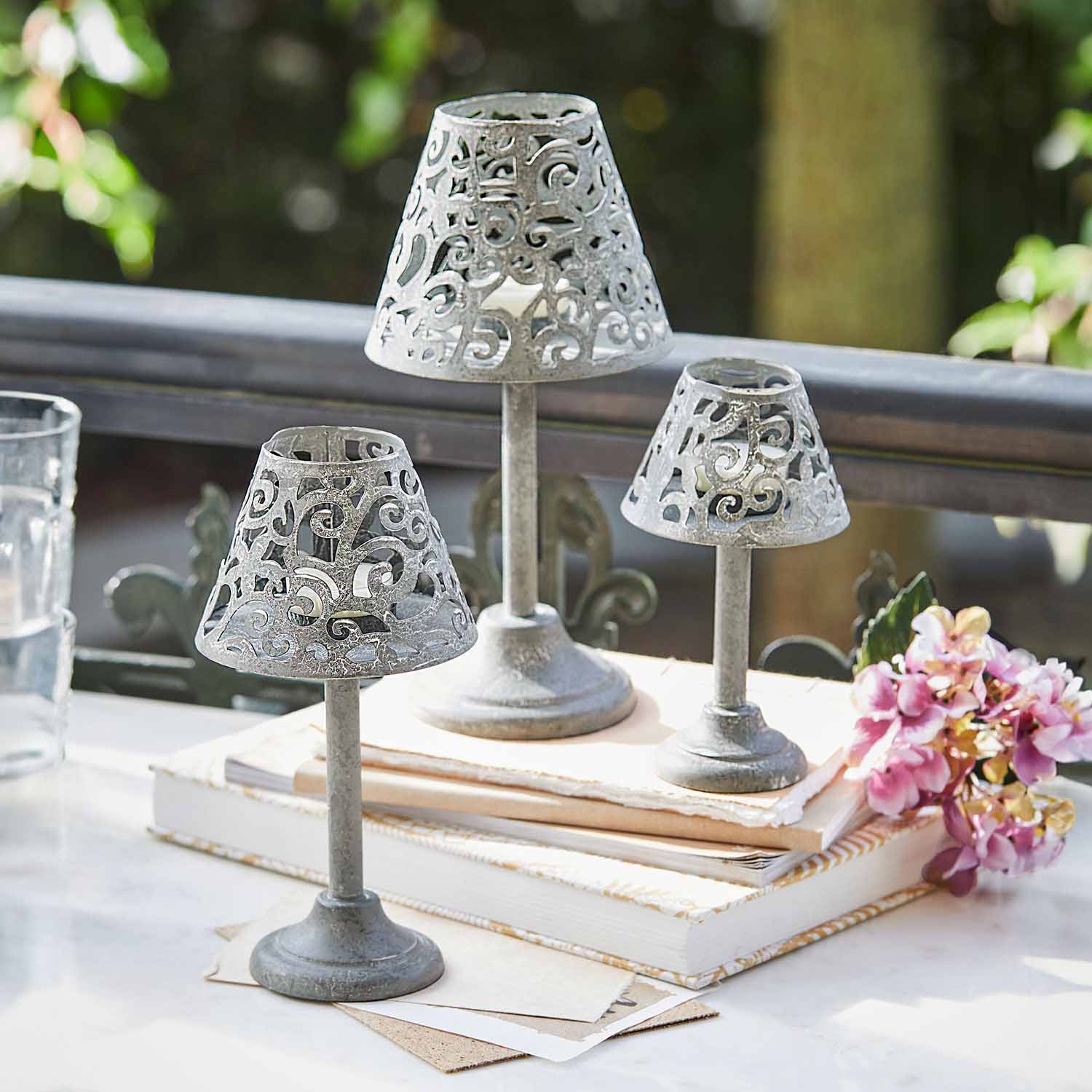 Conjunto de tres candelabros de metal gris con diseño calado sobre libros en una mesa
