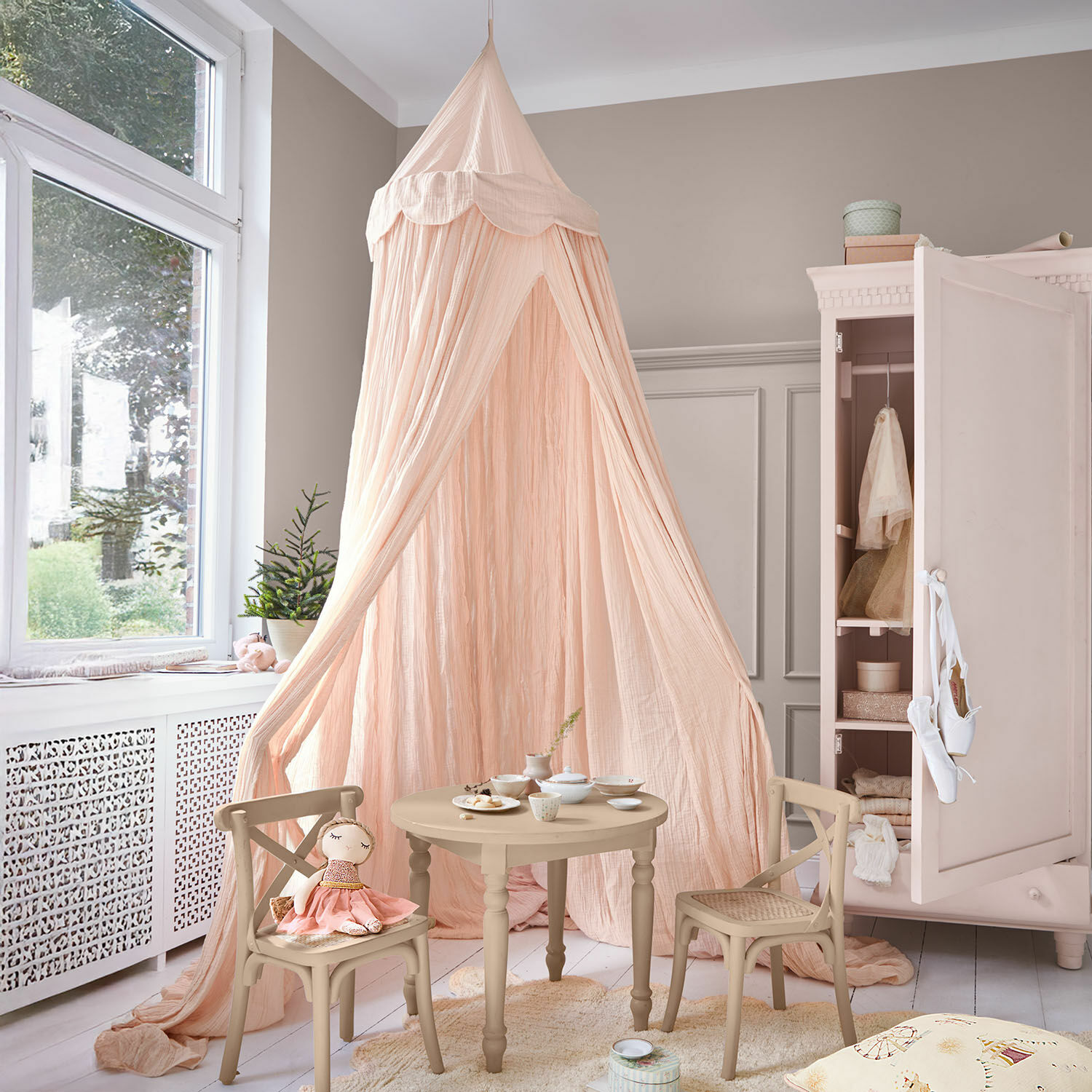 Dosel Larika Habitación infantil con mesa y sillas de madera beige y dosel rosa de tela ligera
