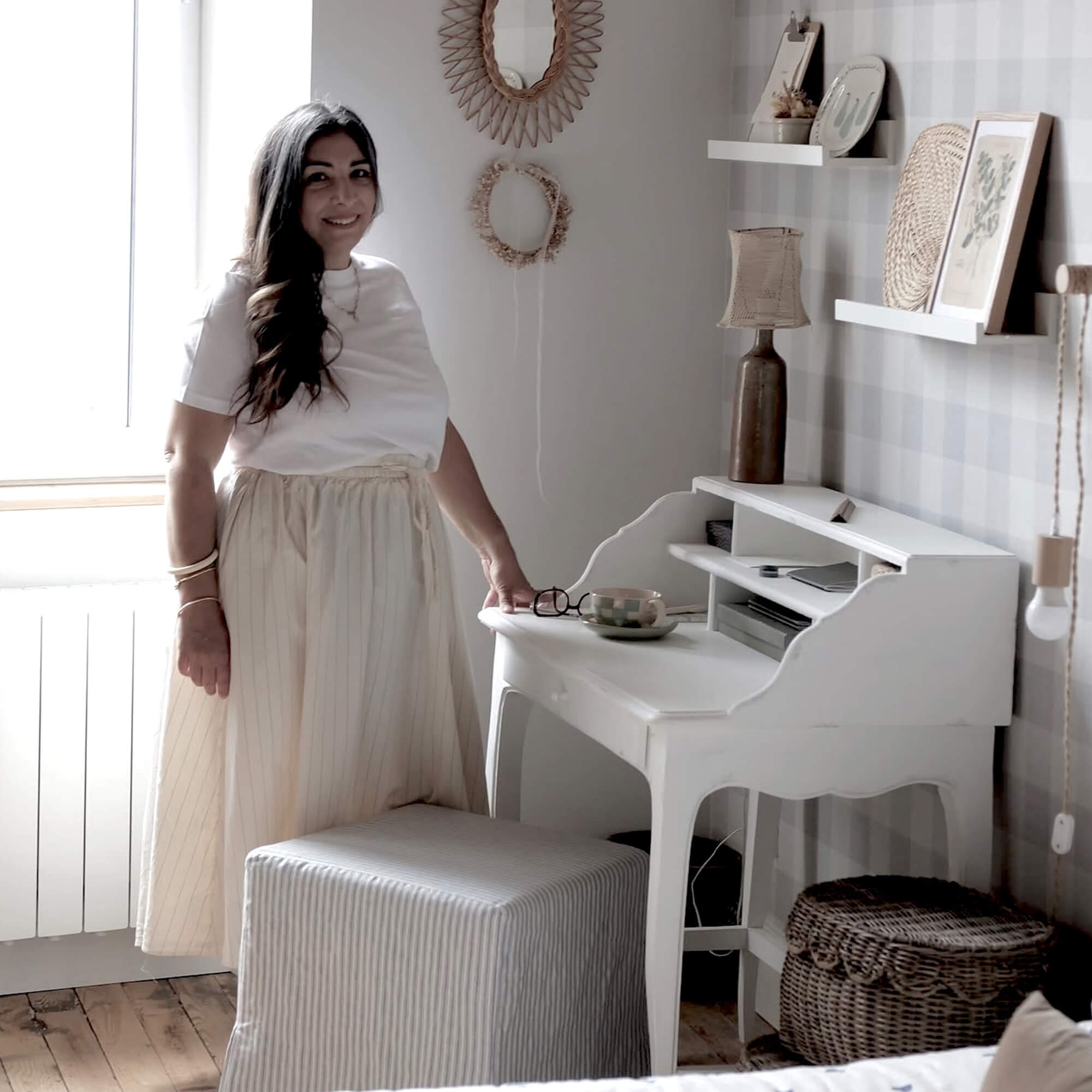 Mujer con falda clara junto a escritorio blanco de madera en habitación acogedora con decoración natural