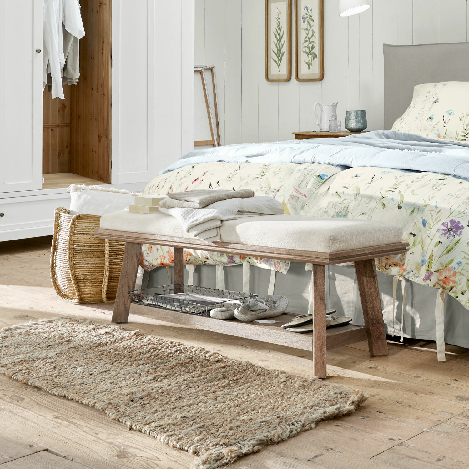Banco de madera con asiento tapizado claro en dormitorio, alfombra natural y decoración floral