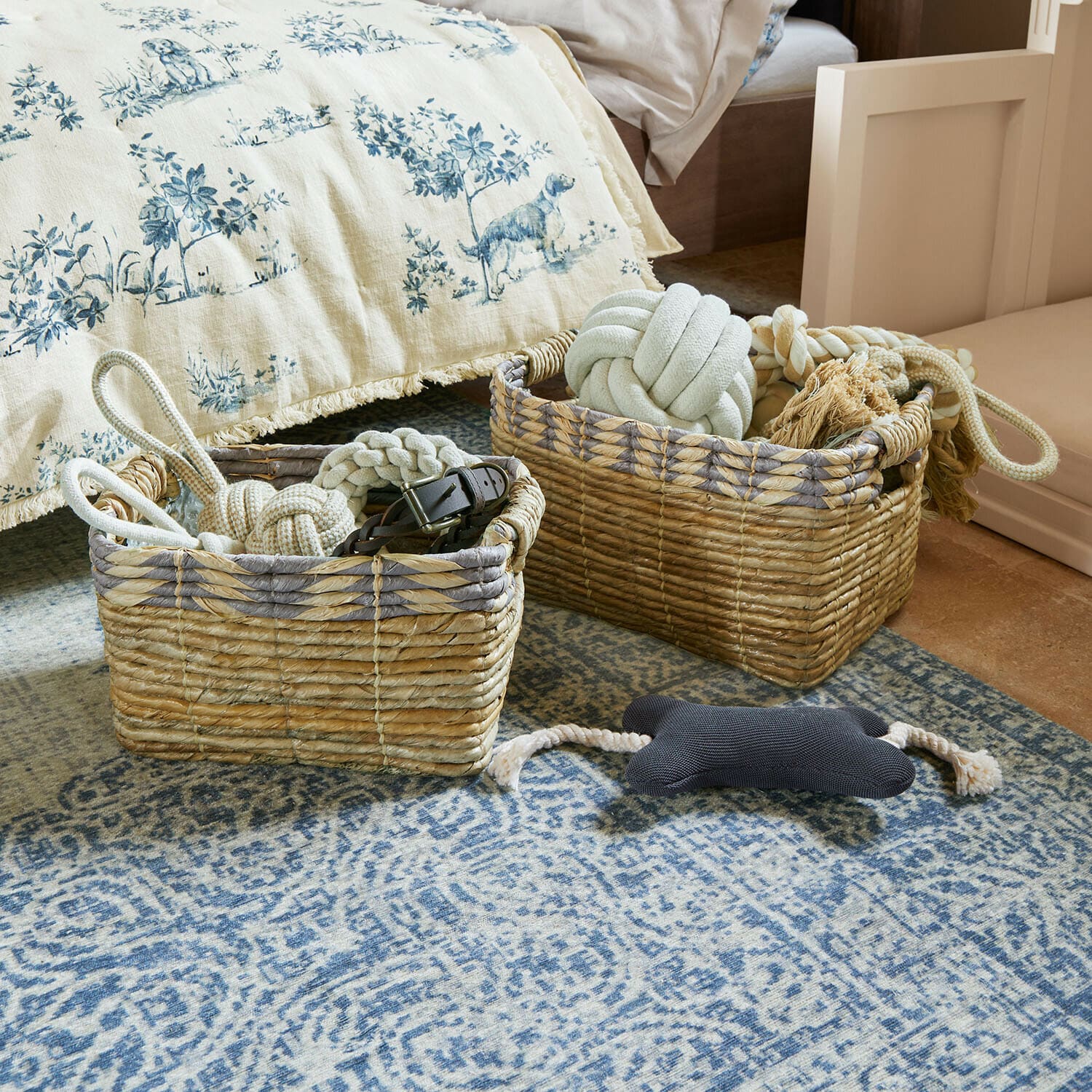 Dos cestas de mimbre natural con juguetes para perros sobre una alfombra azul en dormitorio