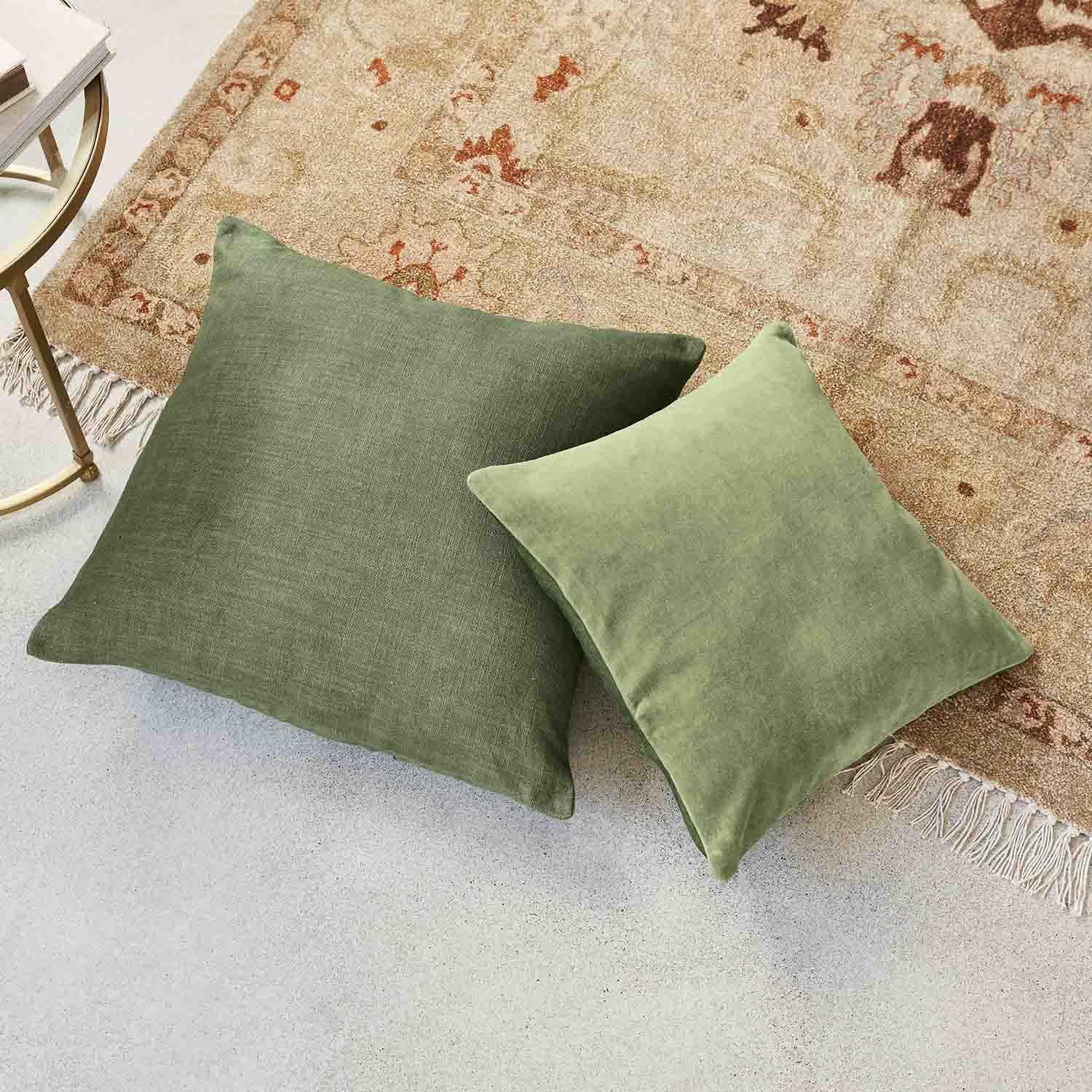 Dos cojines verdes de tela sobre alfombra beige con flecos, accesorios decorativos para salón acogedor