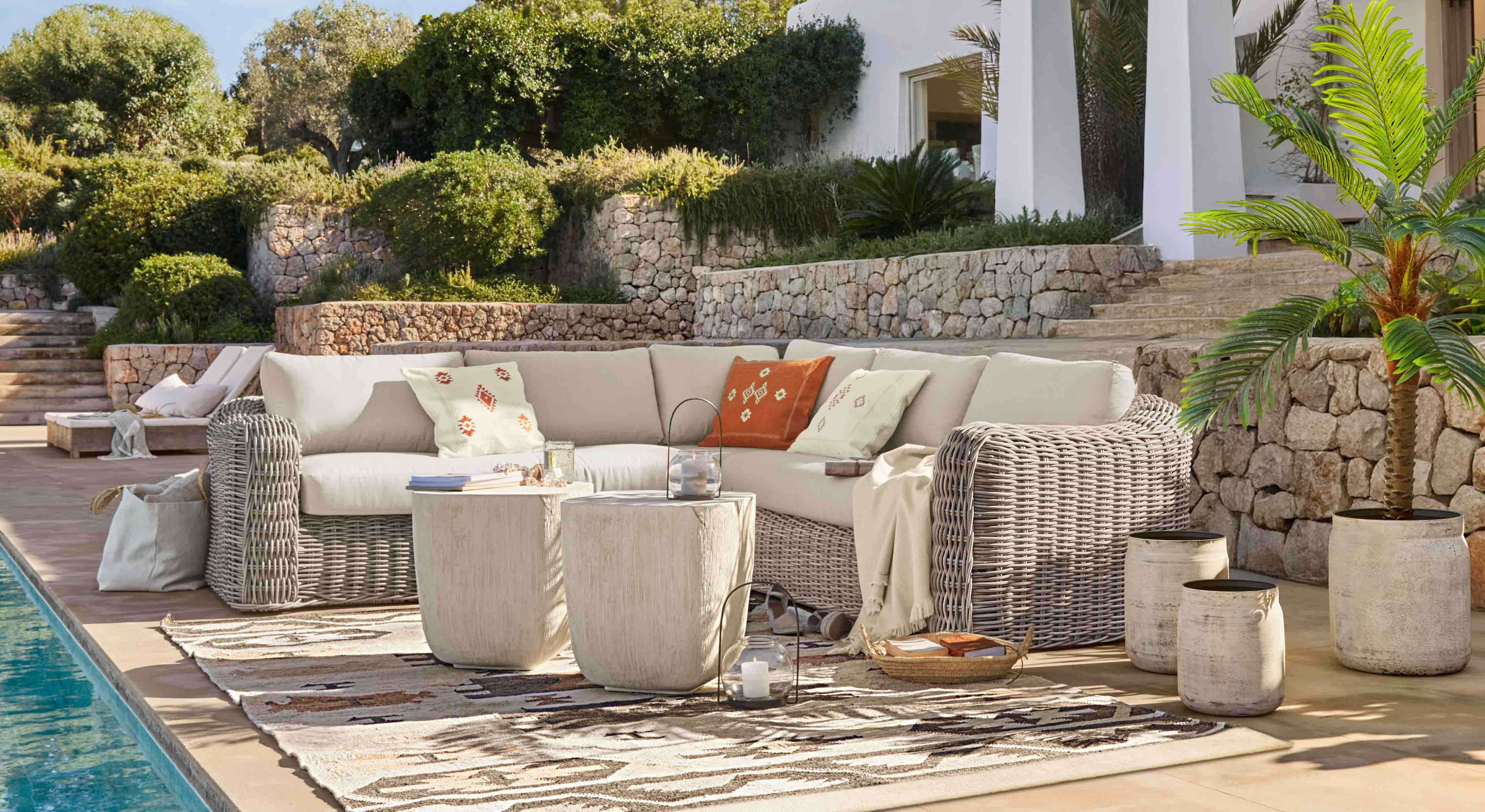 Conjunto de muebles de jardín de ratán gris claro con cojines crema y cojines decorativos en terraza junto a la piscina