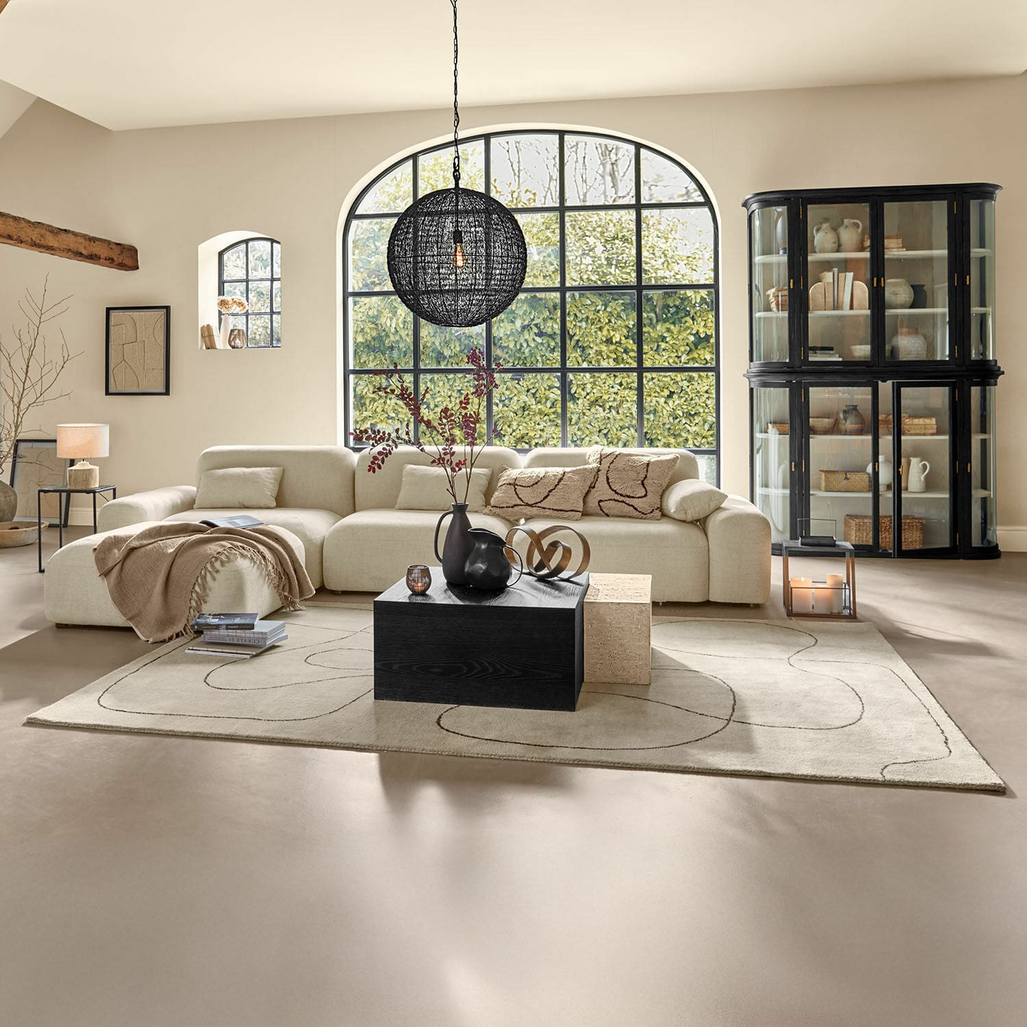 Alfombra Lavinois Sala amplia con sofá beige de tela, mesa de madera negra y gran ventana con vista a la vegetación