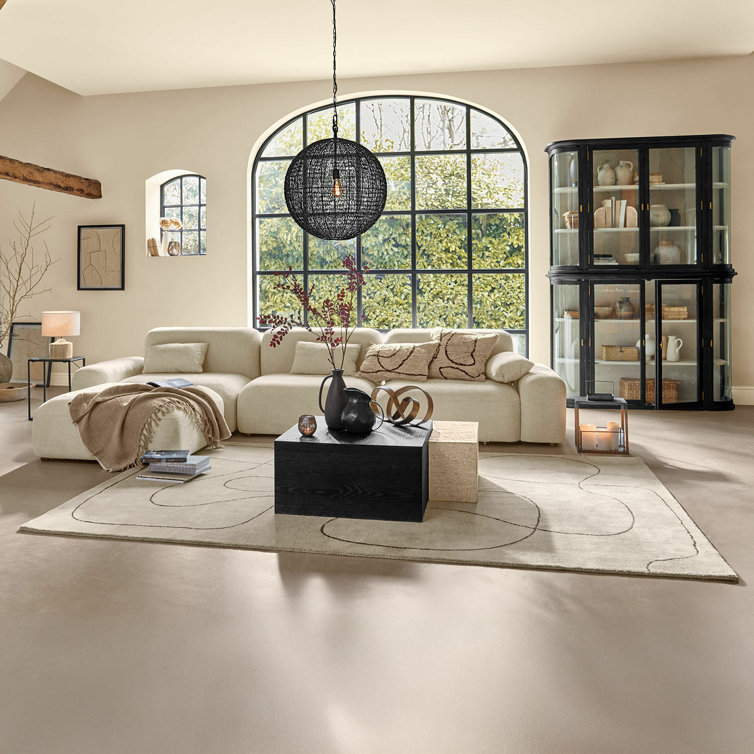 Alfombra Lavinois Sala amplia con sofá beige de tela, mesa de madera negra y gran ventana con vista a la vegetación